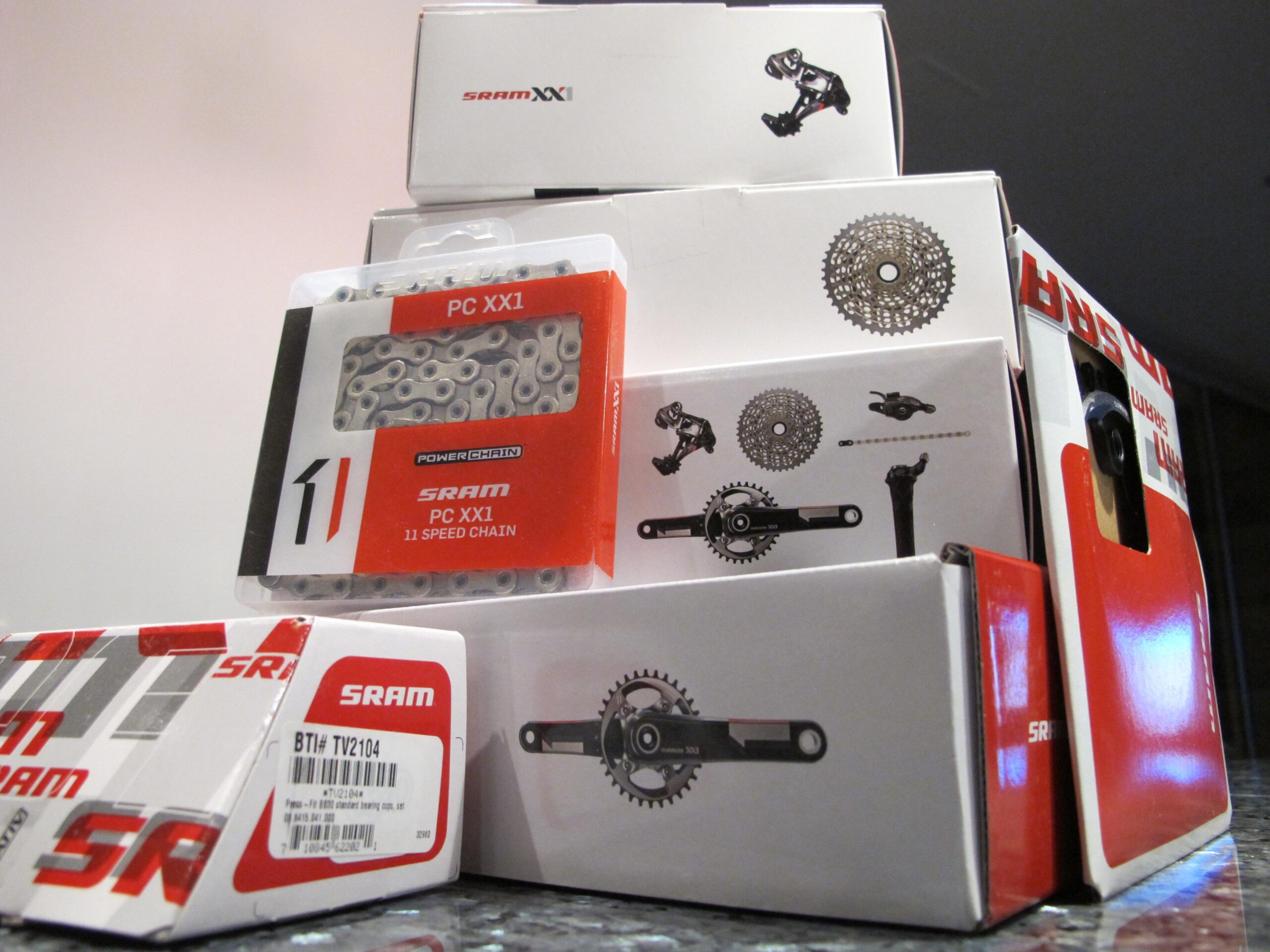 A collection of SRAM bicycle component boxes stacked together, featuring a packaging for a PC XX1 11 speed chain and various other components, all in red and white branding.