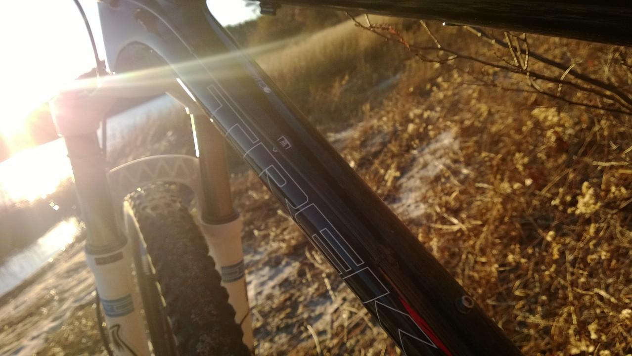 Trek Fuel EX 9.7 29: Alt tag: Close-up of a mountain bike frame with sunlight shining through, surrounded by dry grass and a scenic background.