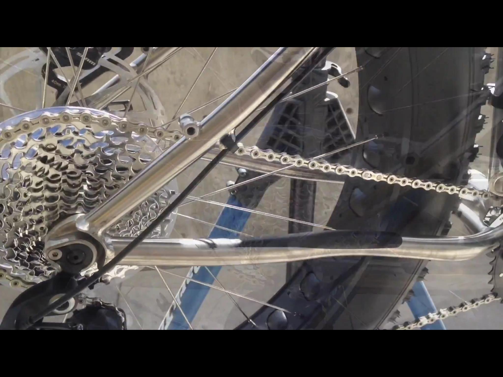 Motobecane Motobecane Bullet Titanium Fat bike: Close-up view of a bicycle's rear wheel assembly, showcasing the shiny metal gears, chain, and part of the frame. The image highlights the intricate design of the drivetrain components, including the cassette and bicycle chain.