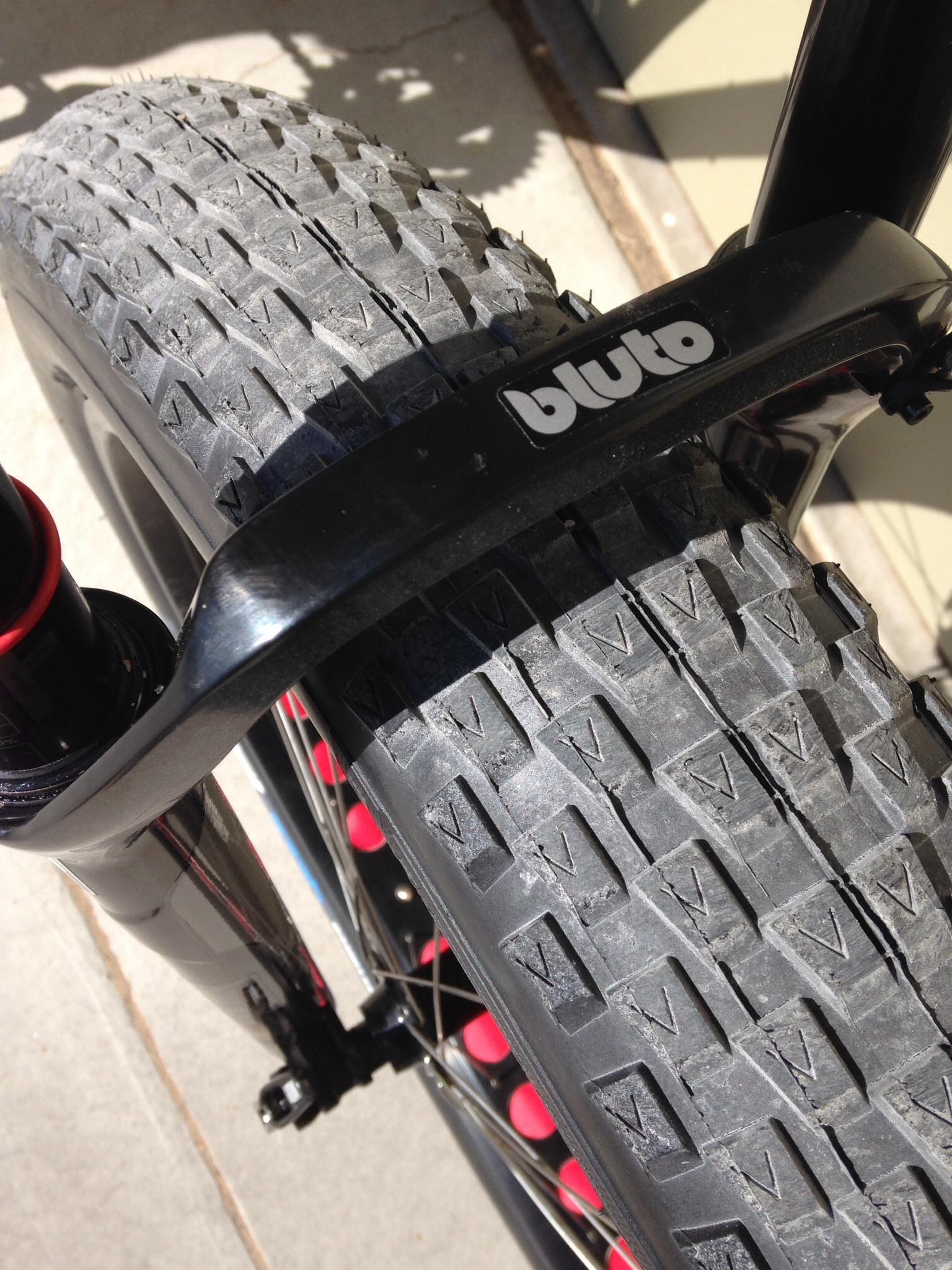 Motobecane Boris: Close-up view of a bicycle tire showcasing its knobby tread pattern, with part of a black bike frame and fender visible in the background. The sunlight creates a clear view of the tire texture and the logo on the fender.