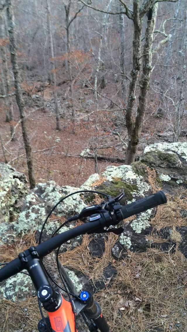 A mountain bike resting on a rocky outcrop in a wooded area, with bare trees and fallen leaves in the background, suggesting a remote outdoor location suitable for biking. Forest City Trail mountain bike trail.
