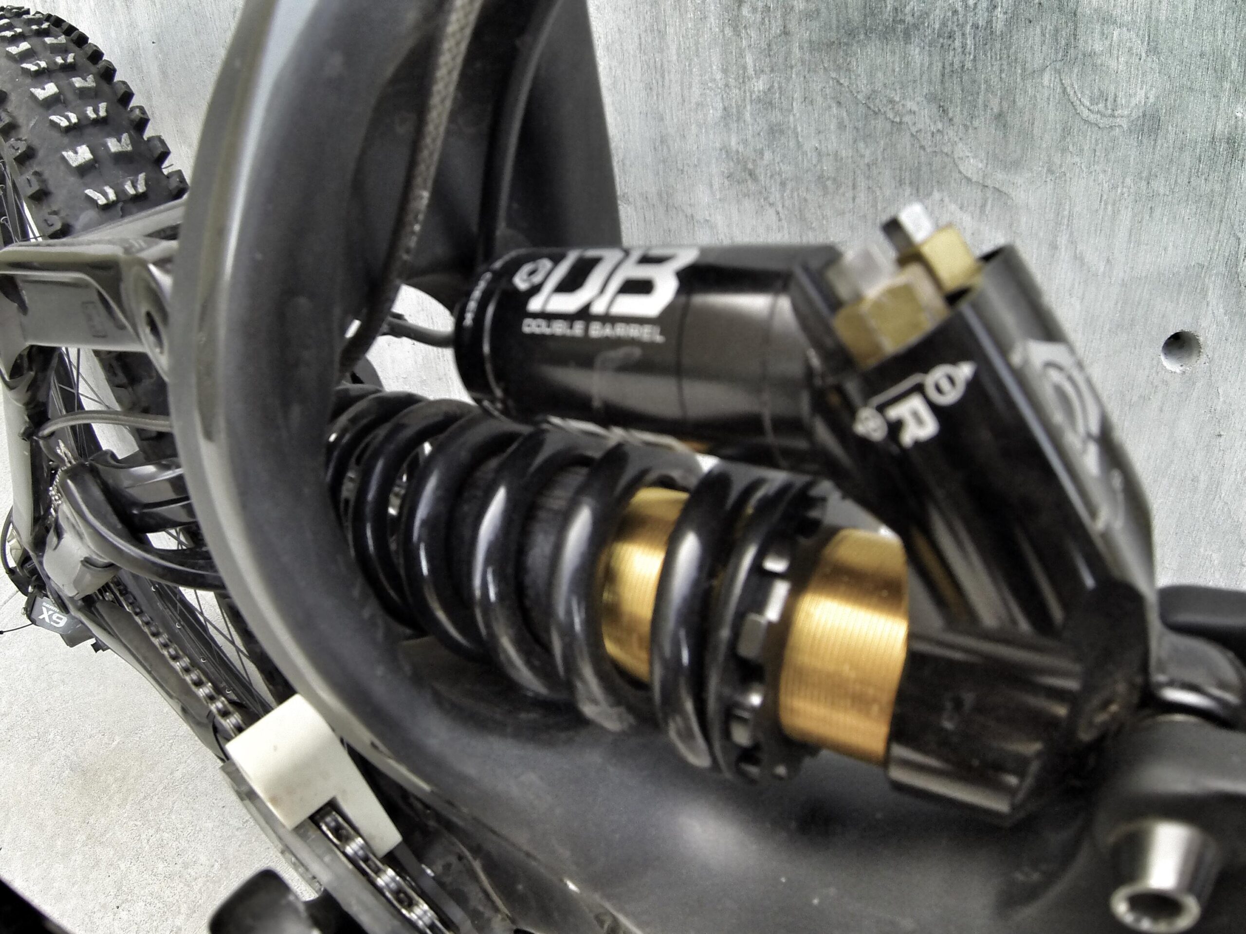 Specialized S-Works Demo 8: Close-up view of a mountain bike shock absorber featuring a black coil spring and a gold barrel body, mounted on the bike's rear suspension frame. The background is a textured gray surface.
