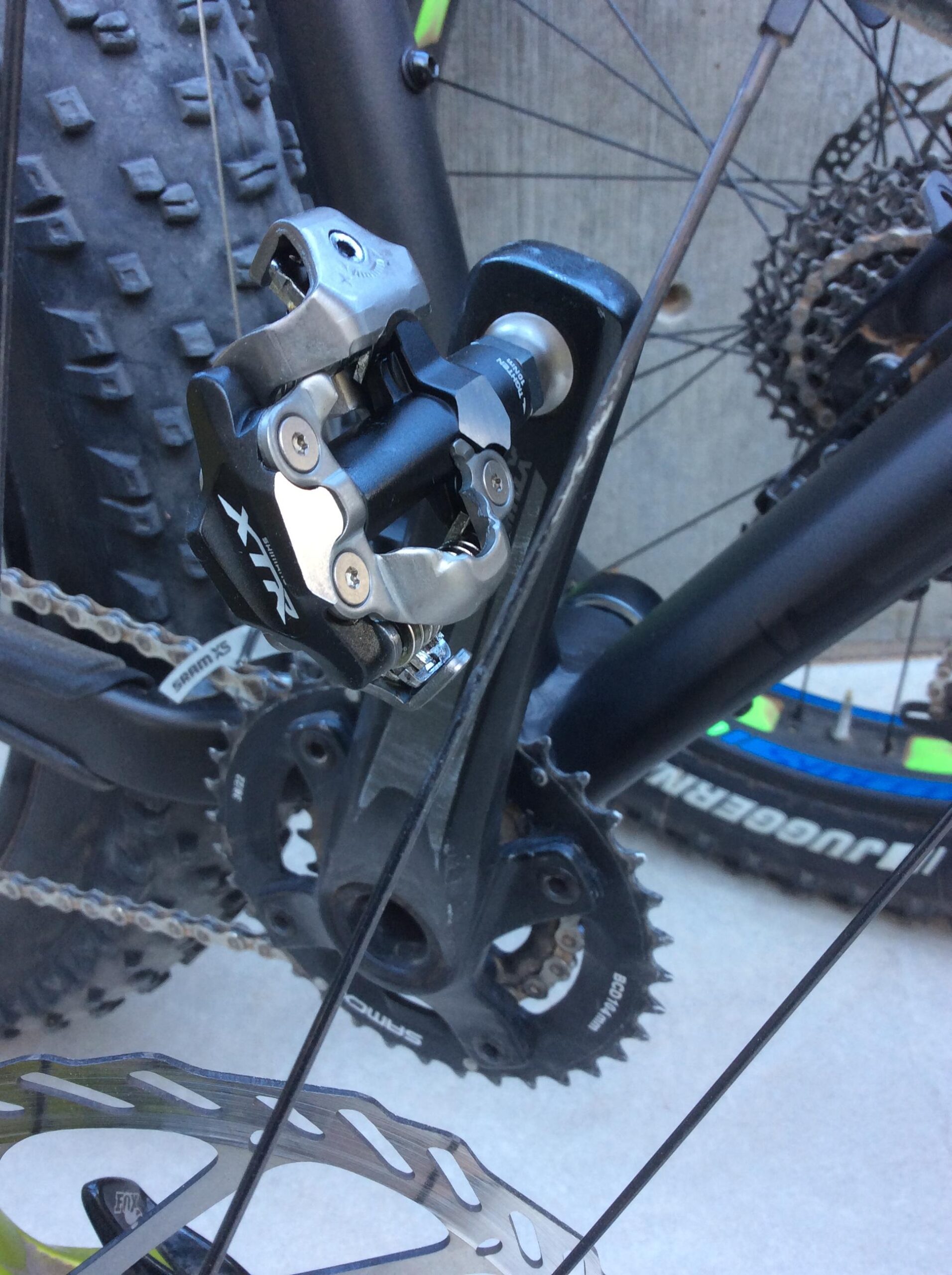Close-up image of a bicycle's rear derailleur, showcasing its metallic components and gears. The bike features a rugged tire in the background, and a portion of the bike frame is visible, highlighting its design. The derailleur is marked with an "XTR" logo, indicating high-performance cycling equipment.