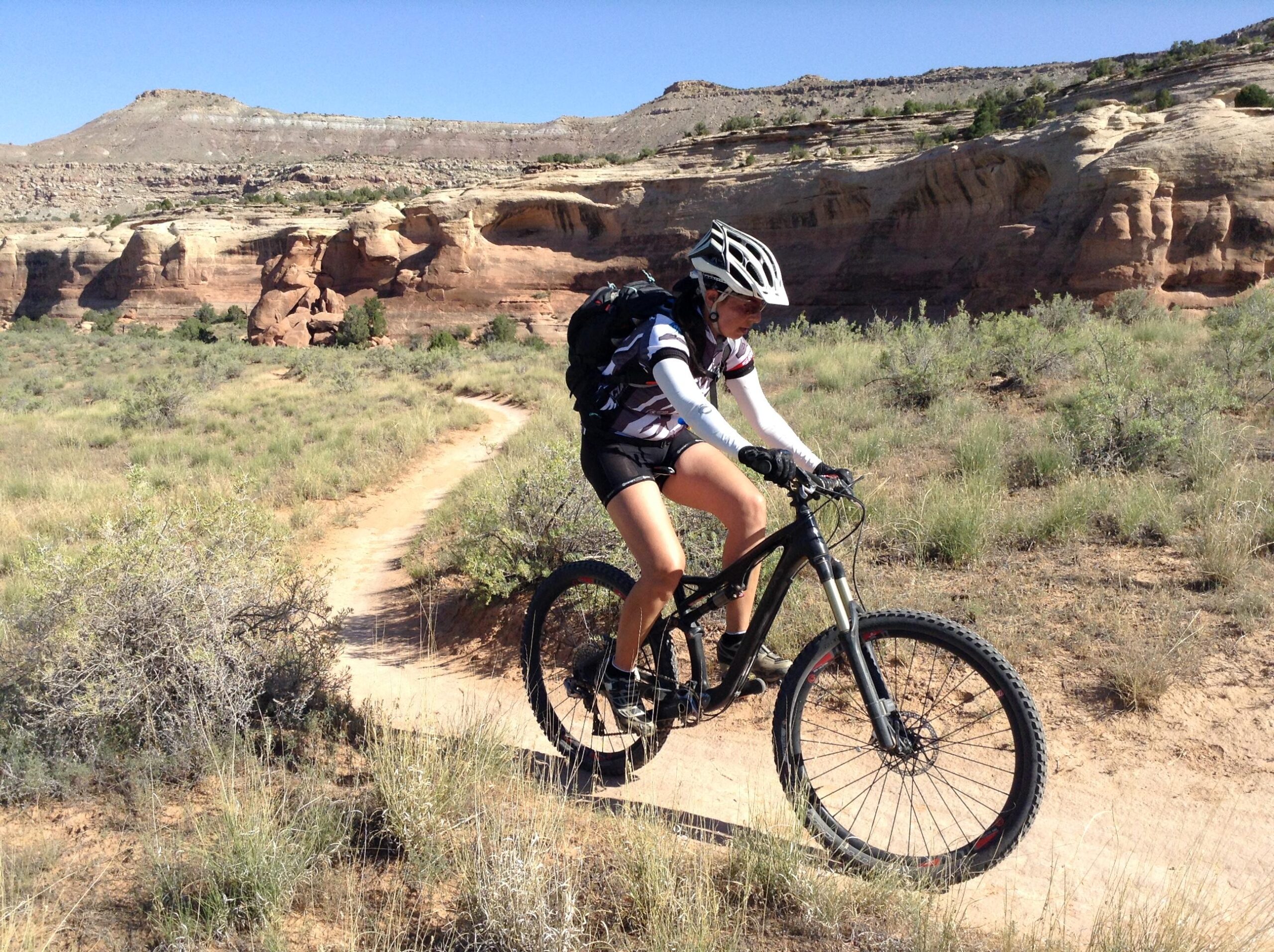 Specialized S-Works Stumpjumper FSR Carbon: A person riding a mountain bike on a dirt trail surrounded by rocky hills and sparse vegetation under a clear blue sky. The rider is wearing a helmet and athletic gear, navigating the winding path through the natural landscape.