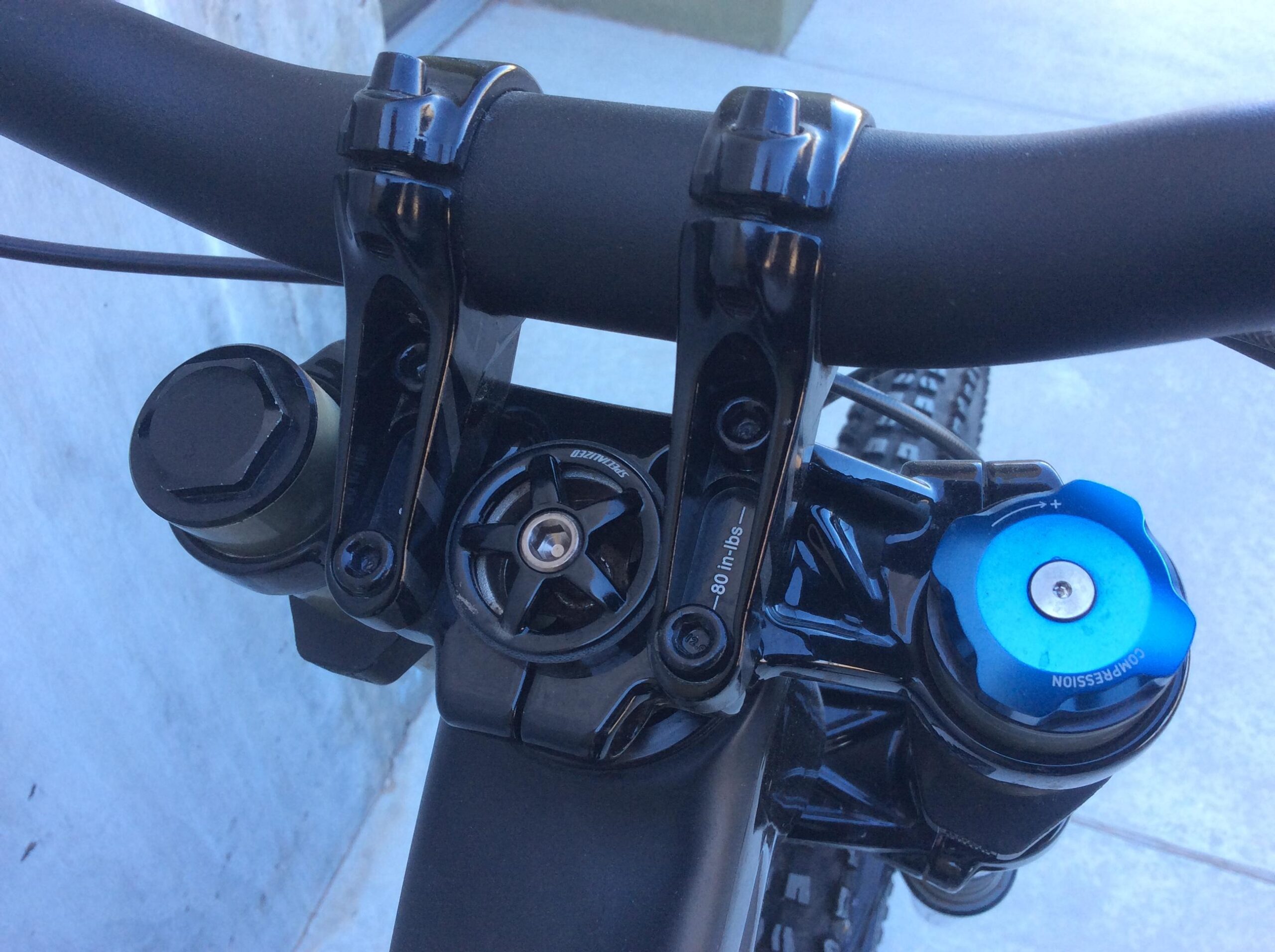 Specialized S-Works Demo 8 Carbon: Close-up view of a mountain bike handlebars setup, showing black handlebar clamps, a compression adjustment knob in blue, and various components of the bike's suspension system.
