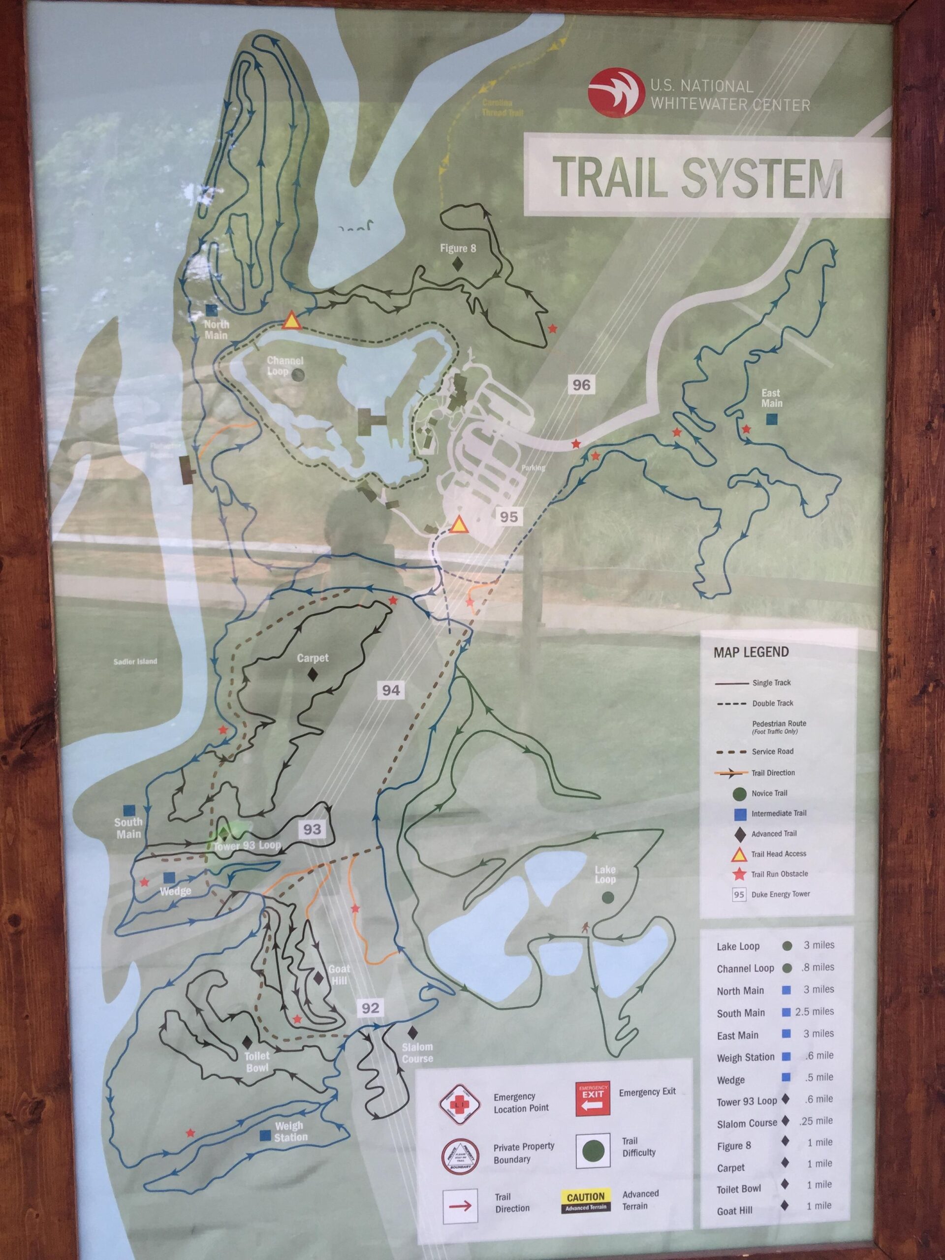 Map of the U.S. National Whitewater Center trail system, featuring various hiking and biking trails. The map includes trail designations, distances, and safety information, highlighting routes such as Lake Loop, Channel Loop, and Goat Hill. It also indicates emergency location points and trail difficulty levels. USNWC mountain bike trail.