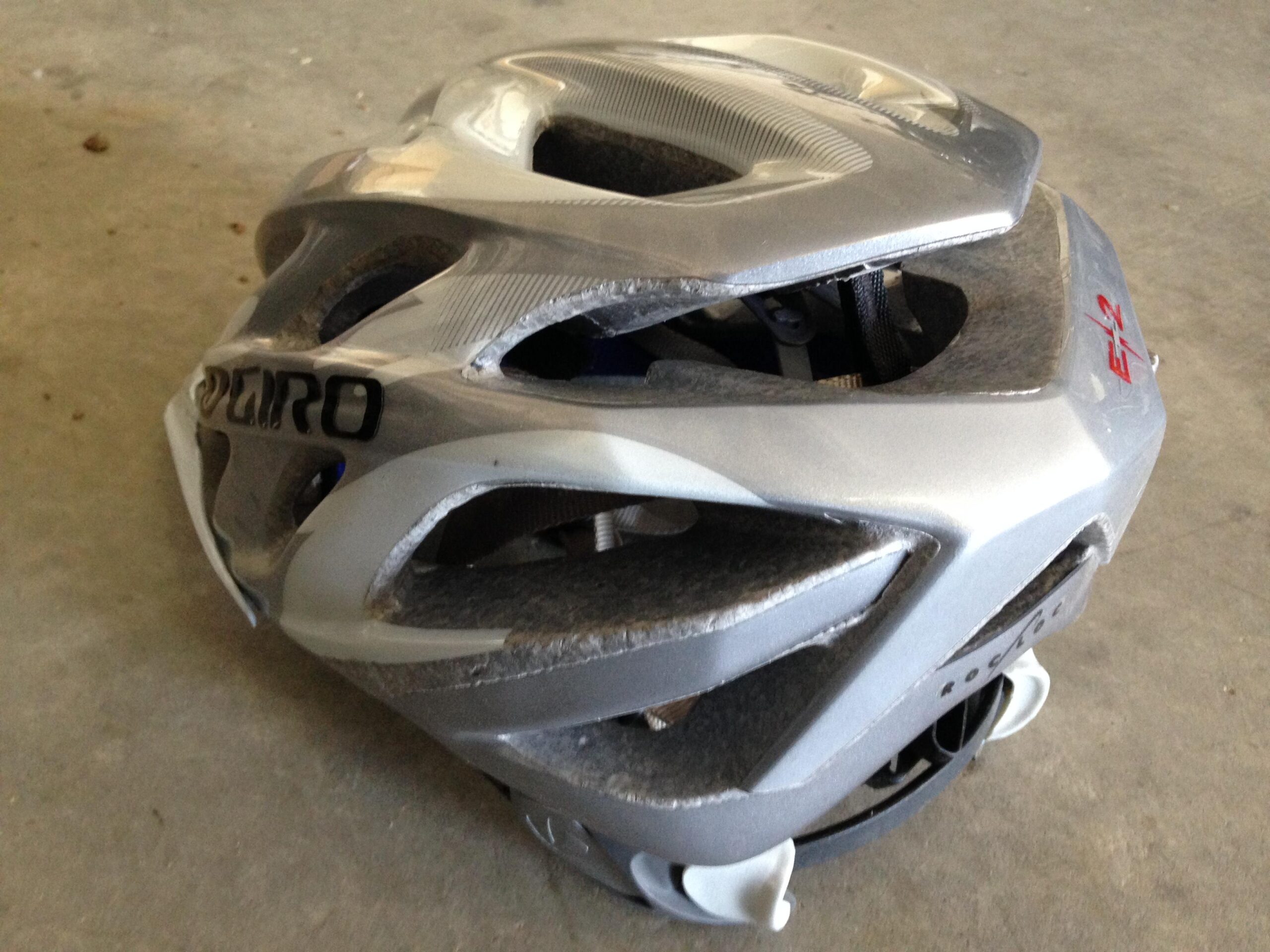 A silver bicycle helmet with ventilation holes resting on a concrete surface. The helmet has a slightly worn appearance and features the logo of the brand "Giro."
