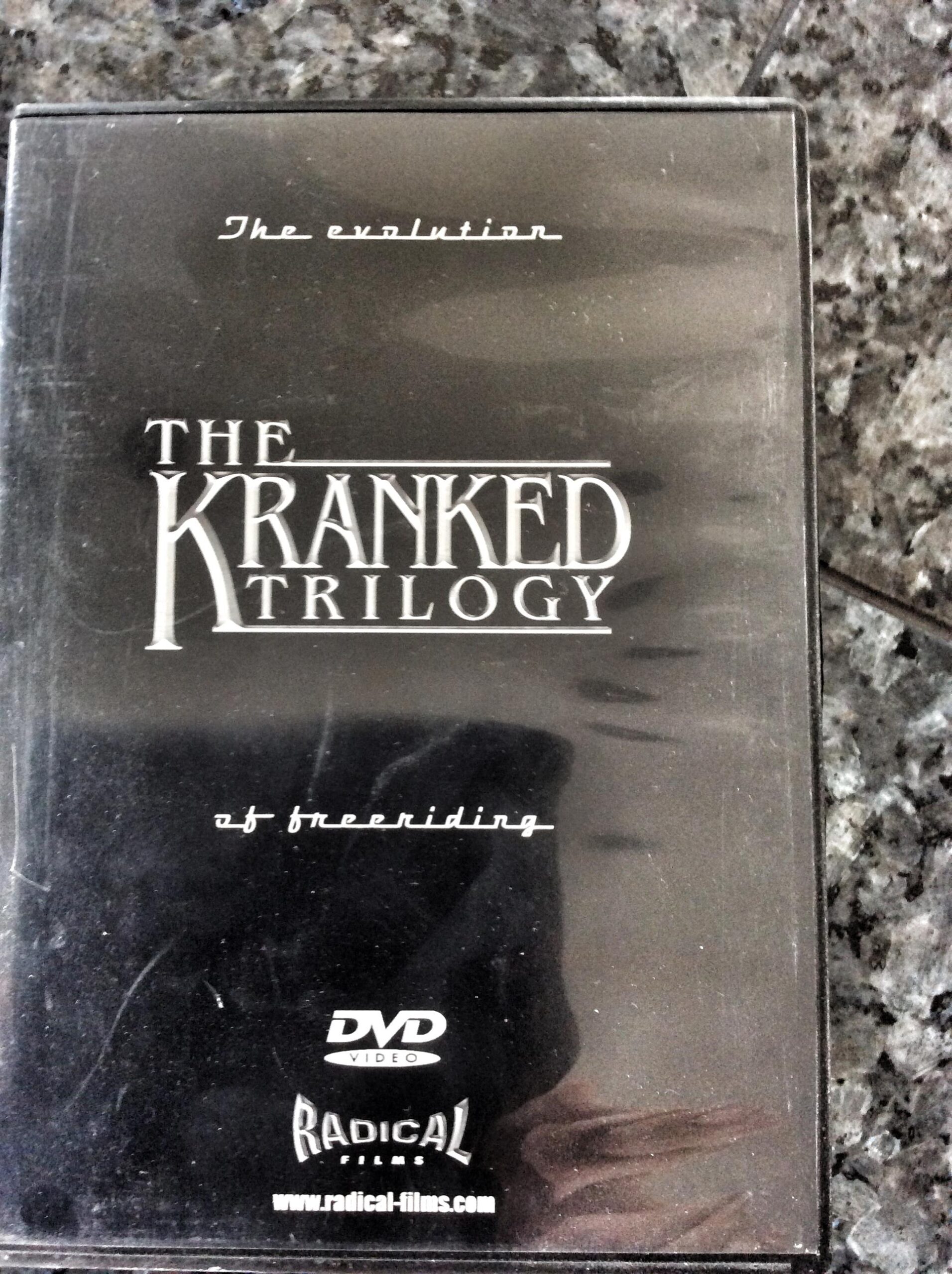 A DVD case featuring "The Kranked Trilogy," with the tagline "The evolution of freeriding." The design is primarily black with white text. The logo for Radical Films is displayed at the bottom, along with the website URL. The case has visible signs of wear.