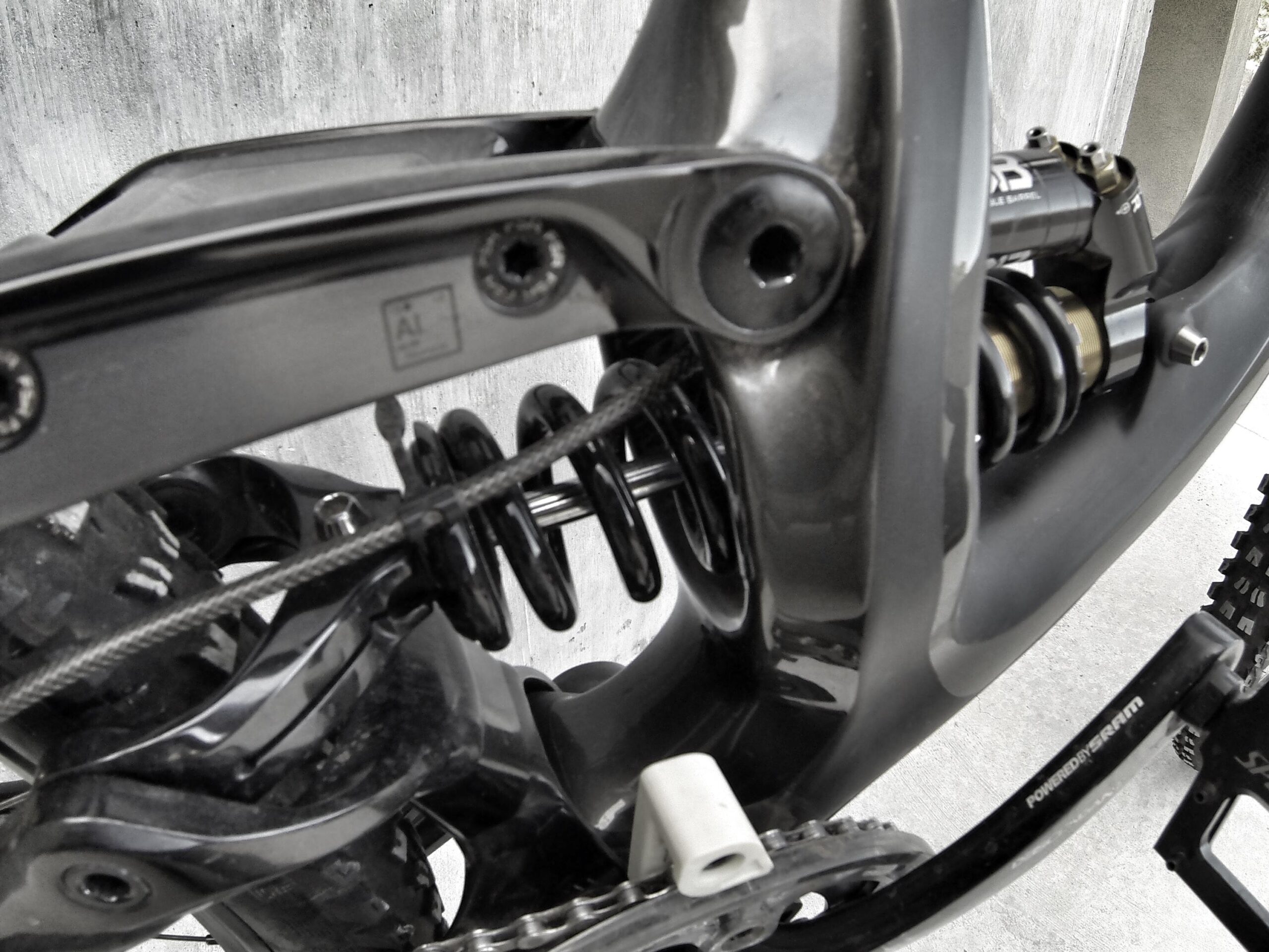 Specialized S-Works Demo 8: Close-up view of a bicycle's rear suspension system, showcasing the coil spring, shock absorber, and chainring. The image highlights the intricate design and engineering of the bike frame, with a textured background.