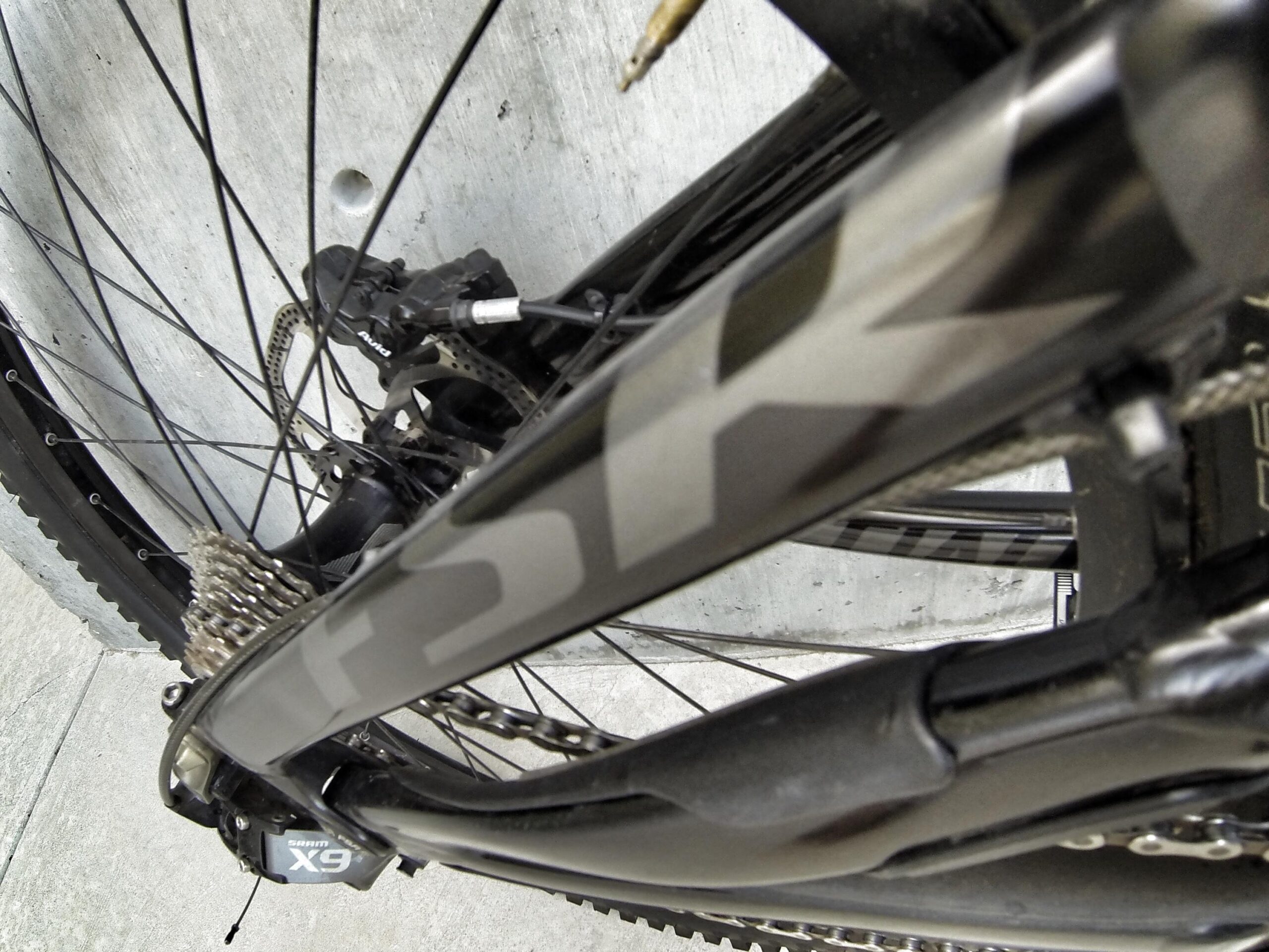 Specialized S-Works Demo 8: Close-up of a mountain bike's rear gears and frame, showcasing the chain, cassette, and derailleur against a concrete surface. The bike features a dark color scheme with the brand name partially visible.