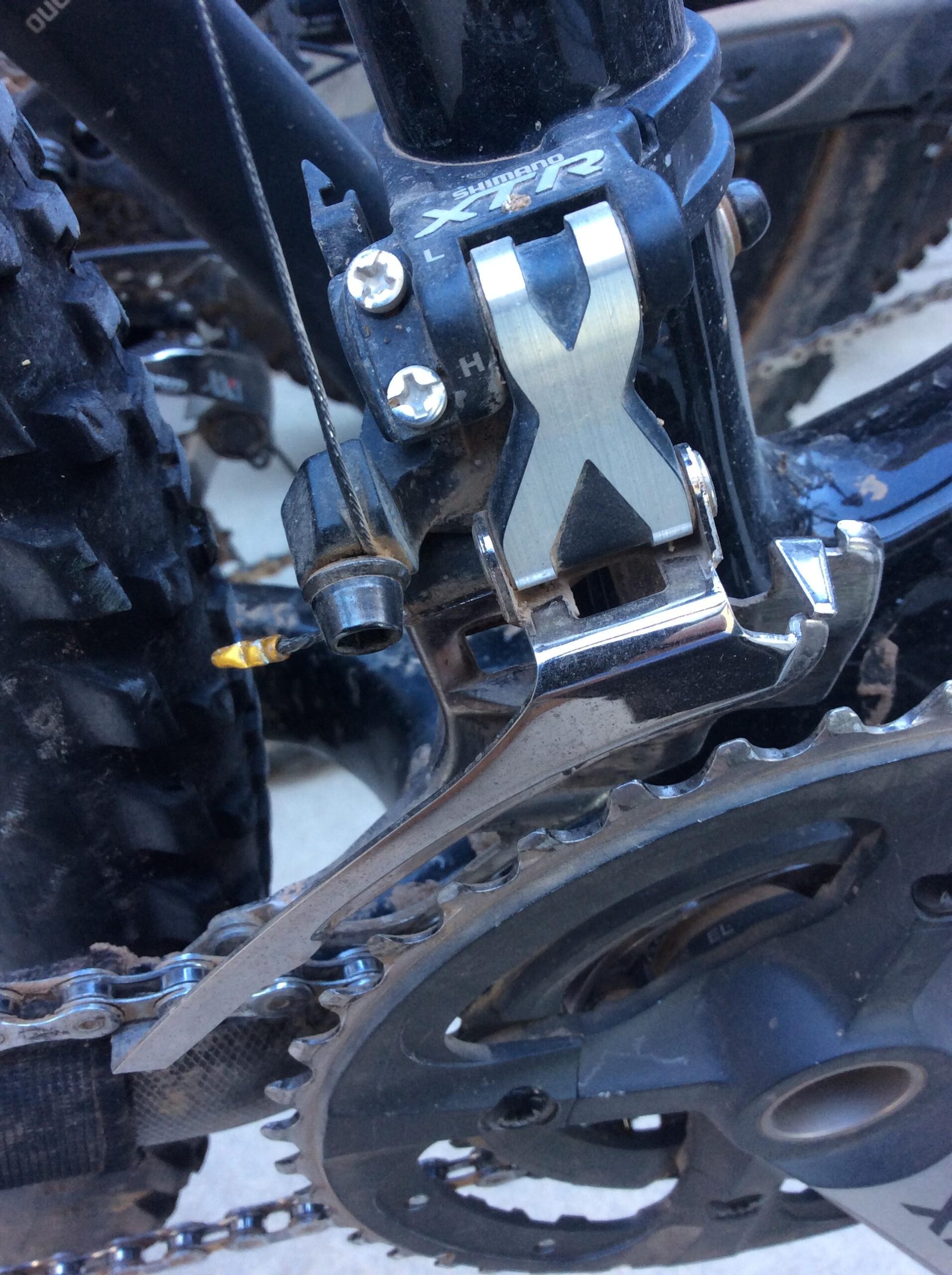 Close-up of a Shimano XT rear derailleur mounted on a mountain bike, showcasing the metal shift lever and chainrings, with visible dirt and wear indicators on the components.