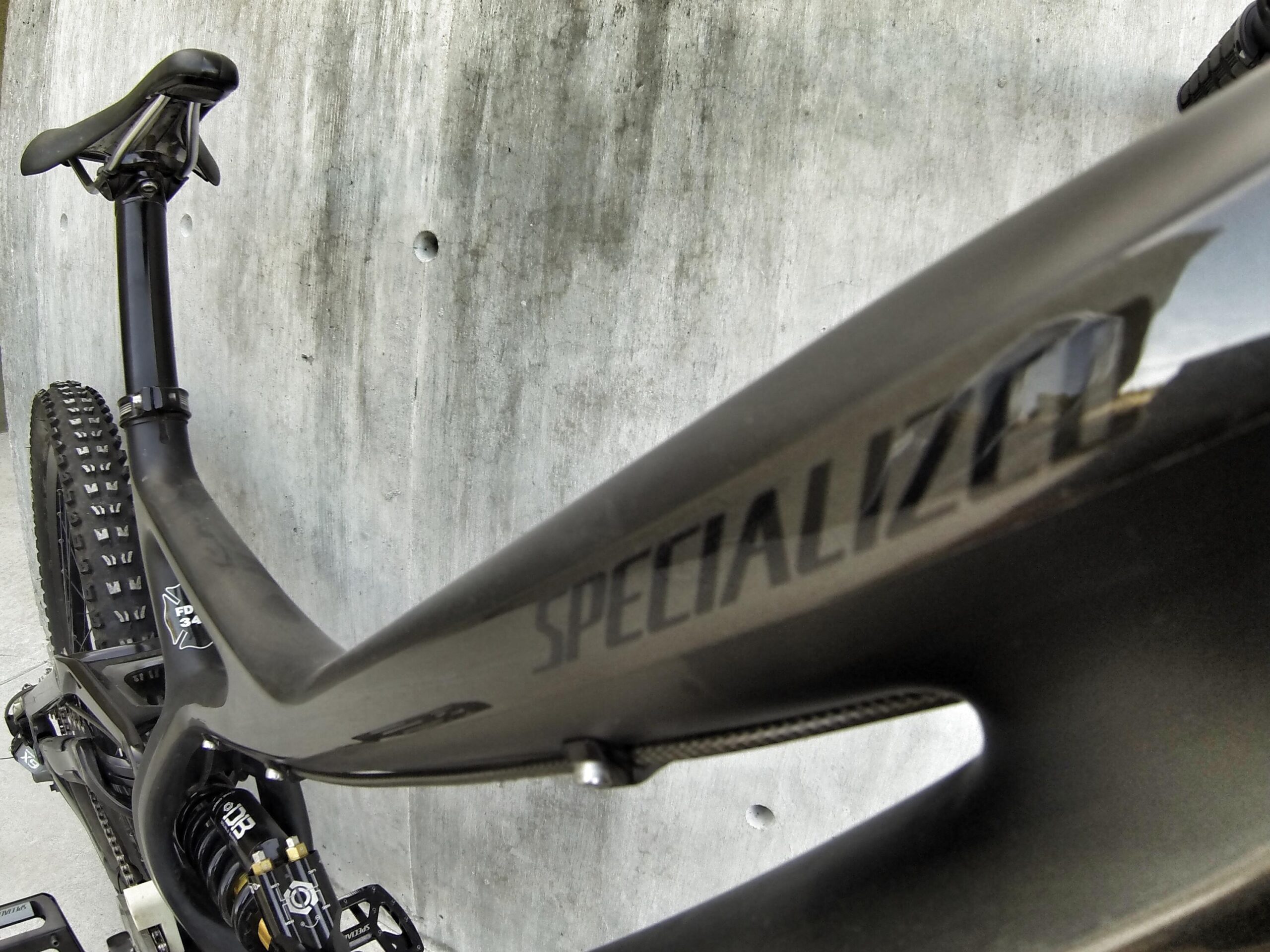 Specialized S-Works Demo 8: Close-up image of a black Specialized mountain bike frame, showcasing the intricate design and detailing, with a textured concrete wall in the background. The focus is on the frame's branding and components, highlighting its sleek structure and off-road capabilities.