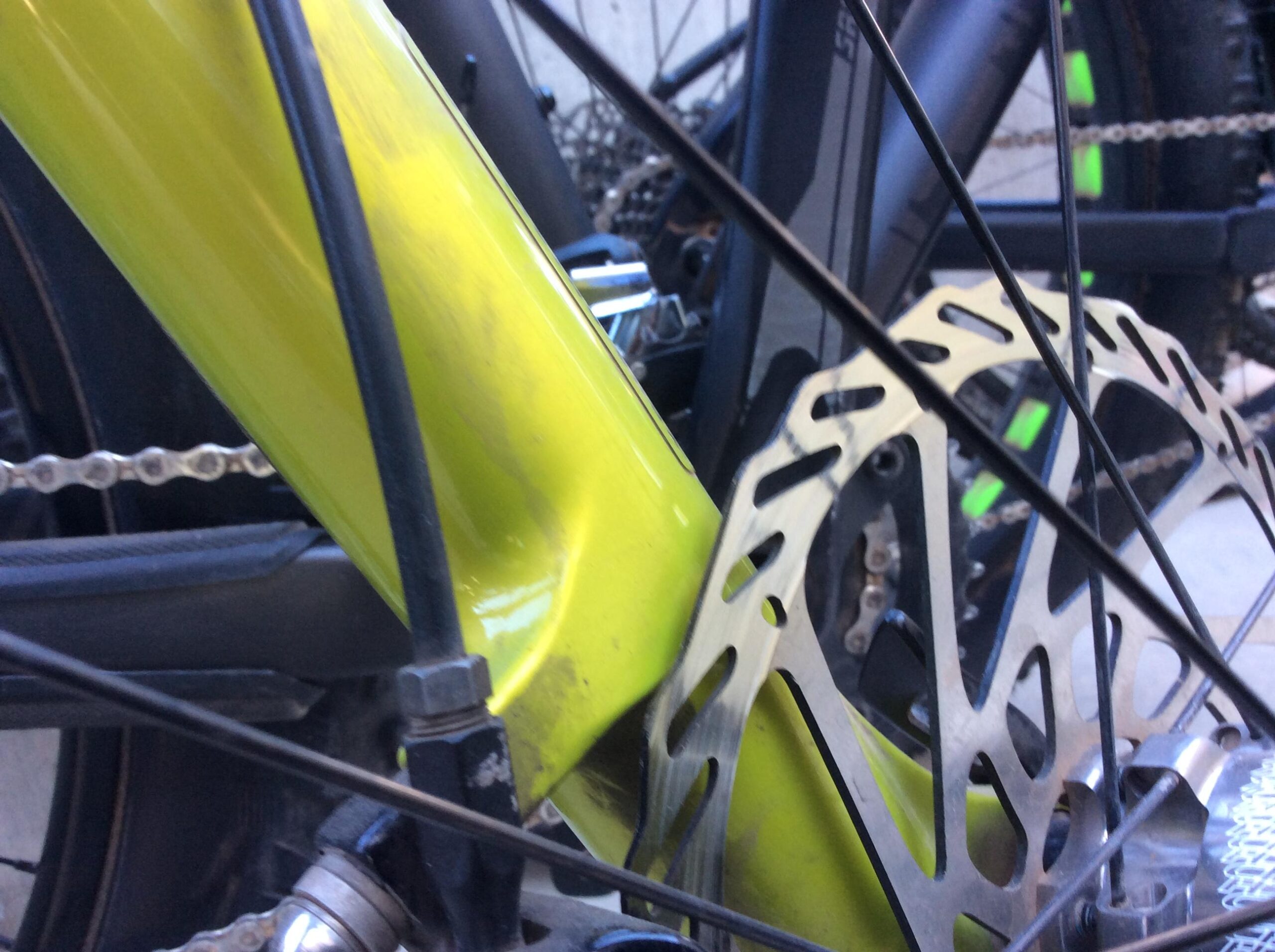 Close-up view of a bright yellow bicycle frame and brake rotor, highlighting the bike's components, including the chain and spokes in the background.