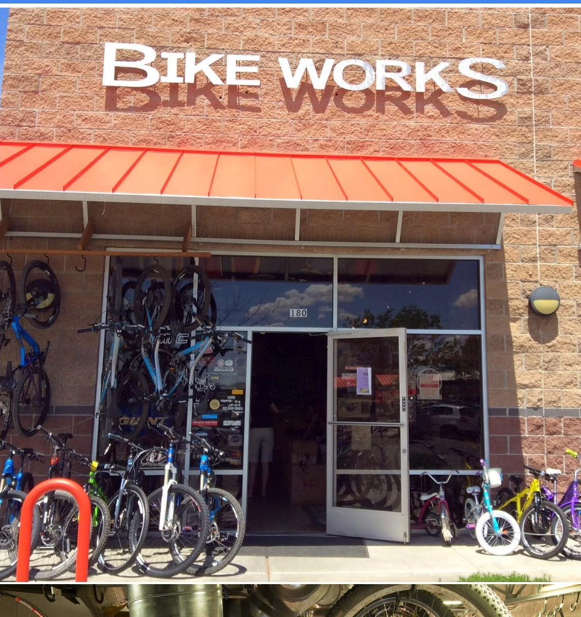 Front entrance of a bike shop named "Bike Works," featuring a variety of bicycles displayed outside. The store has large windows and a red awning, with multiple bikes of different colors parked in front. The shop's signage is clearly visible above the entrance.