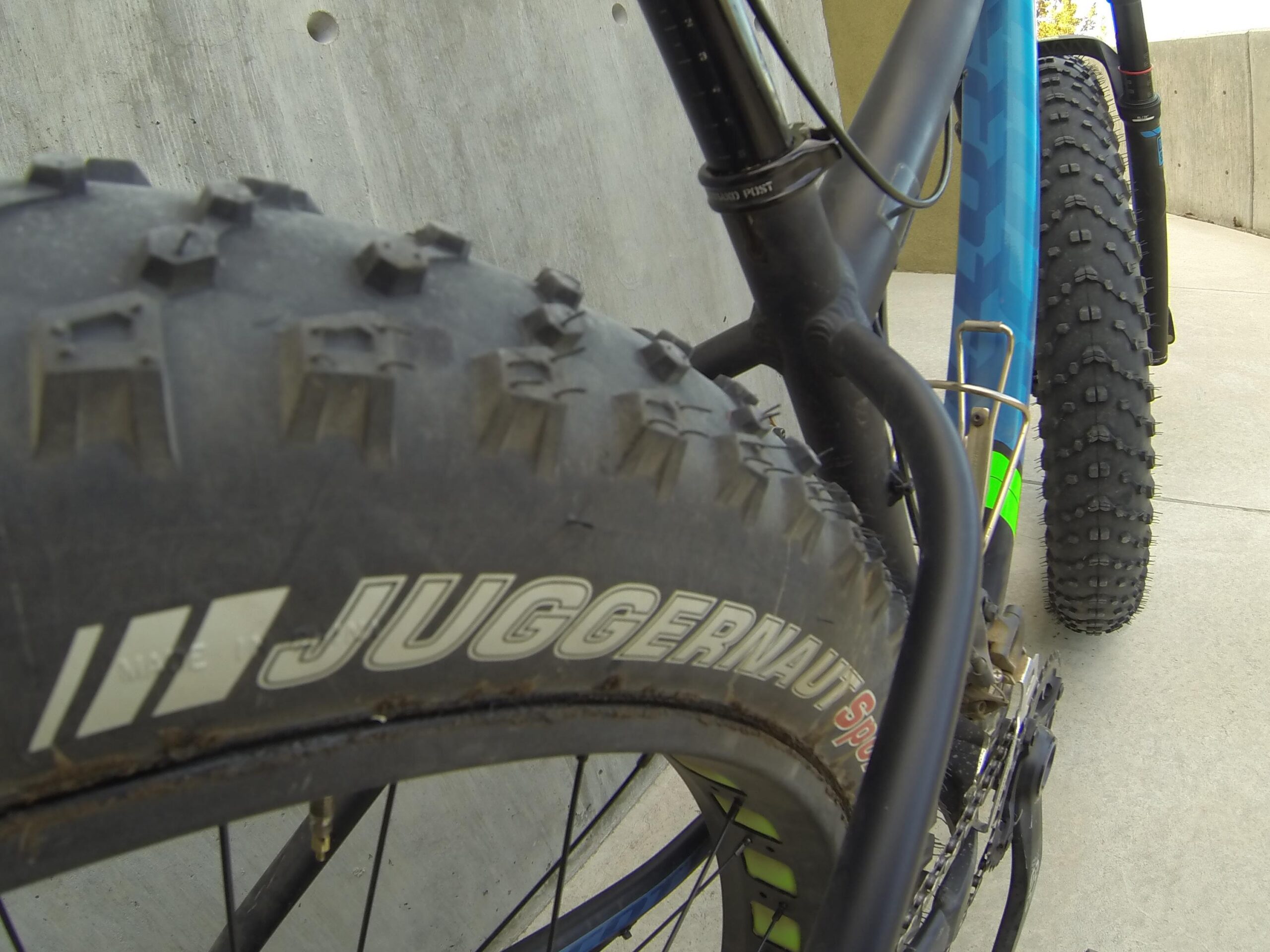 Scott Big Ed: Close-up view of a bicycle's rear tire, highlighting the tread pattern and the brand name "Juggernaut." The background includes part of the bicycle frame and a concrete surface.