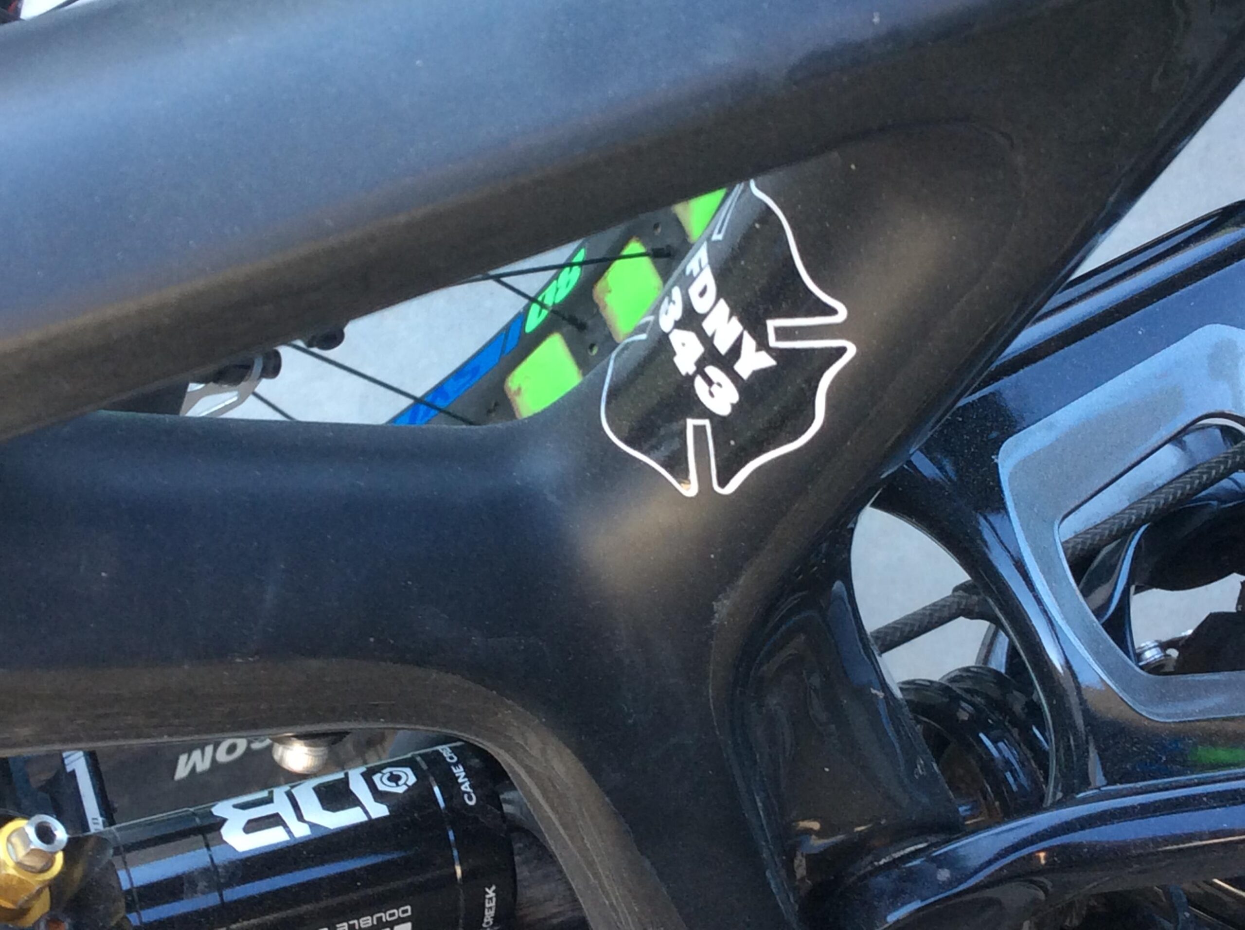 Close-up image of a bicycle frame featuring a black and white sticker with the text "FDNY 343," symbolizing tribute or support. The background includes parts of the bike, showcasing its components and design.