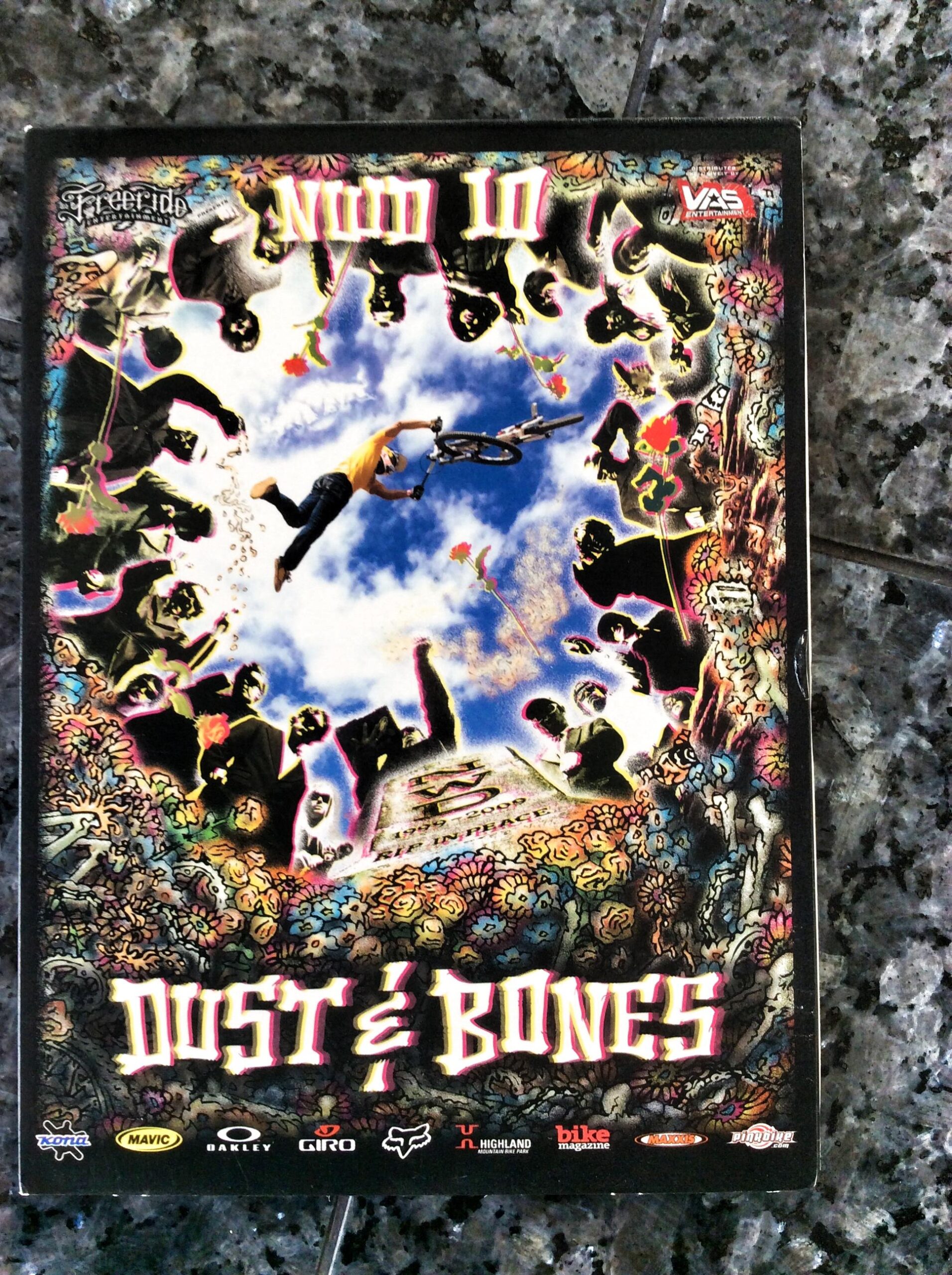 A colorful DVD cover for "Dust & Bones" featuring a central image of a cyclist performing a trick against a vibrant blue sky, surrounded by a border of stylized figures and floral designs. The title is prominently displayed at the bottom, with various logos of sponsors along the bottom edge.