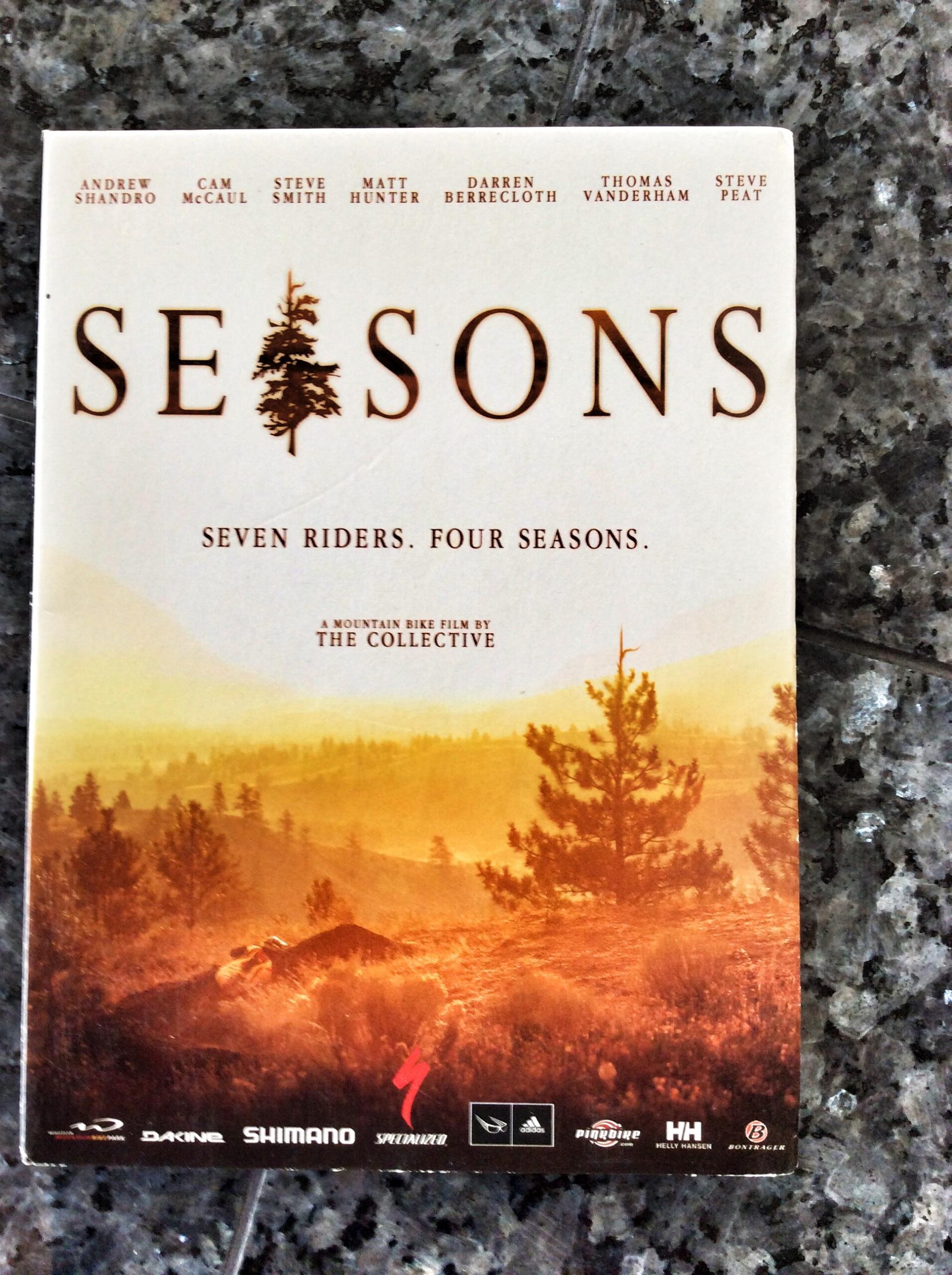 Alt text: Cover of the mountain bike film "Seasons" featuring the title in bold letters, a forest silhouette, and text indicating "Seven riders. Four seasons." The film is presented by The Collective and includes the names of featured riders.