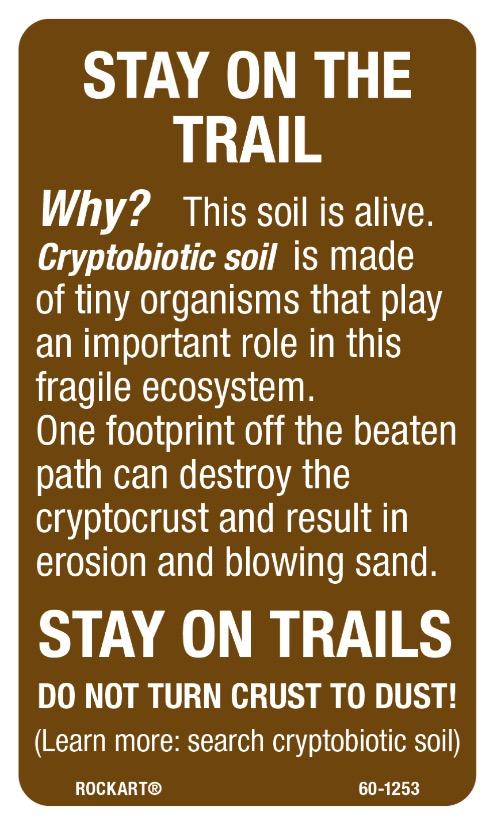 A informational sign emphasizing the importance of staying on designated trails to protect fragile cryptobiotic soil, detailing how this soil hosts vital tiny organisms. The sign warns that stepping off trails can damage the ecosystem, cause erosion, and lead to blowing sand. It features bold titles and calls to action, urging visitors to "Stay on Trails" and "Do Not Turn Crust to Dust." White Ridge Bike Trails mountain bike trail.