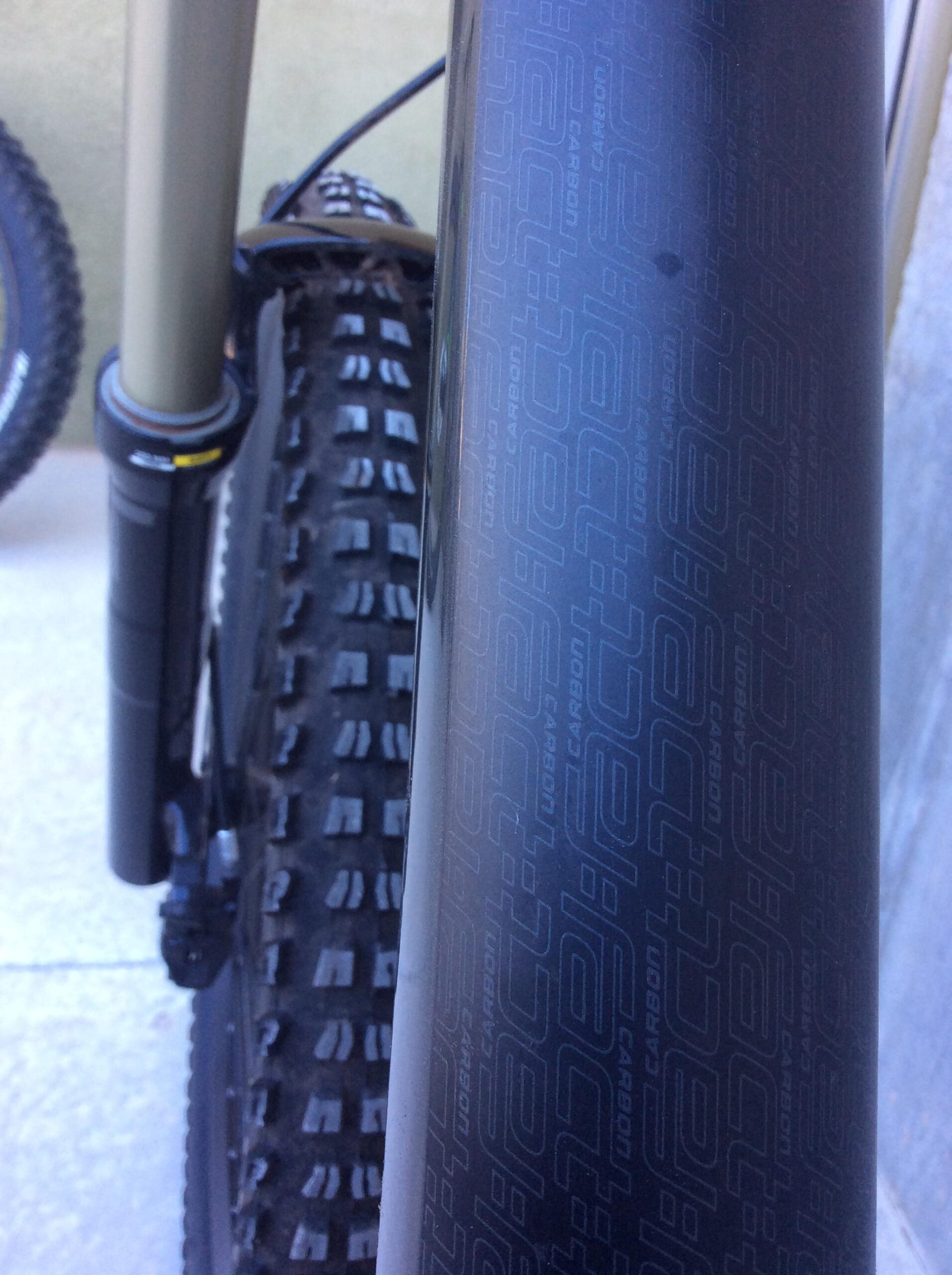 Specialized S-Works Demo 8 Carbon: Close-up view of a bicycle's front tire and fork, showcasing a textured tire tread and a carbon fiber frame with branding details visible. The background features another tire and part of the bike, with a smooth surface underneath.