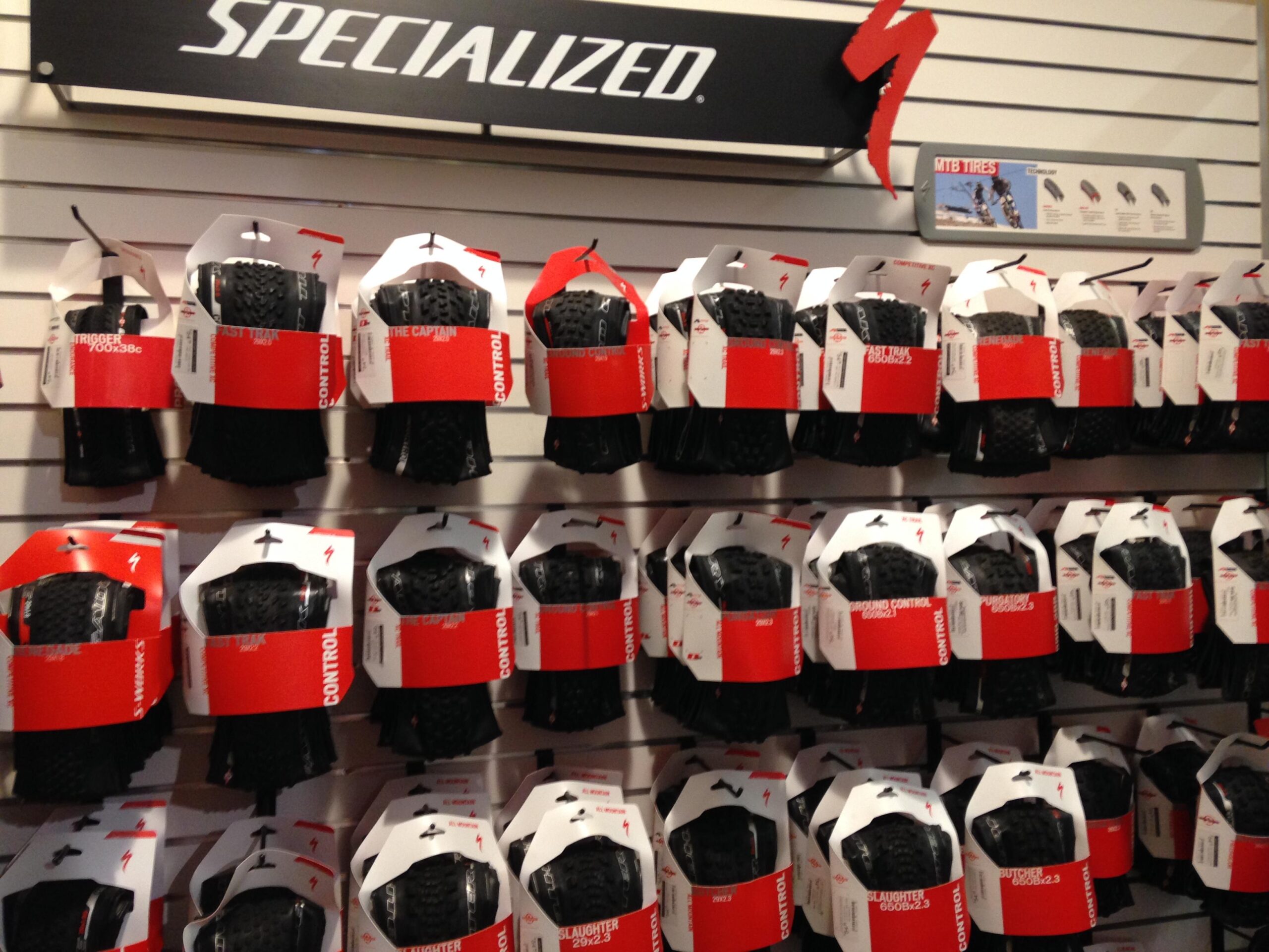 A display wall showcasing various mountain bike tires from the brand Specialized, with packaging clearly labeled for different tire models. The products are arranged in rows, each with a red and white design, against a neutral background.