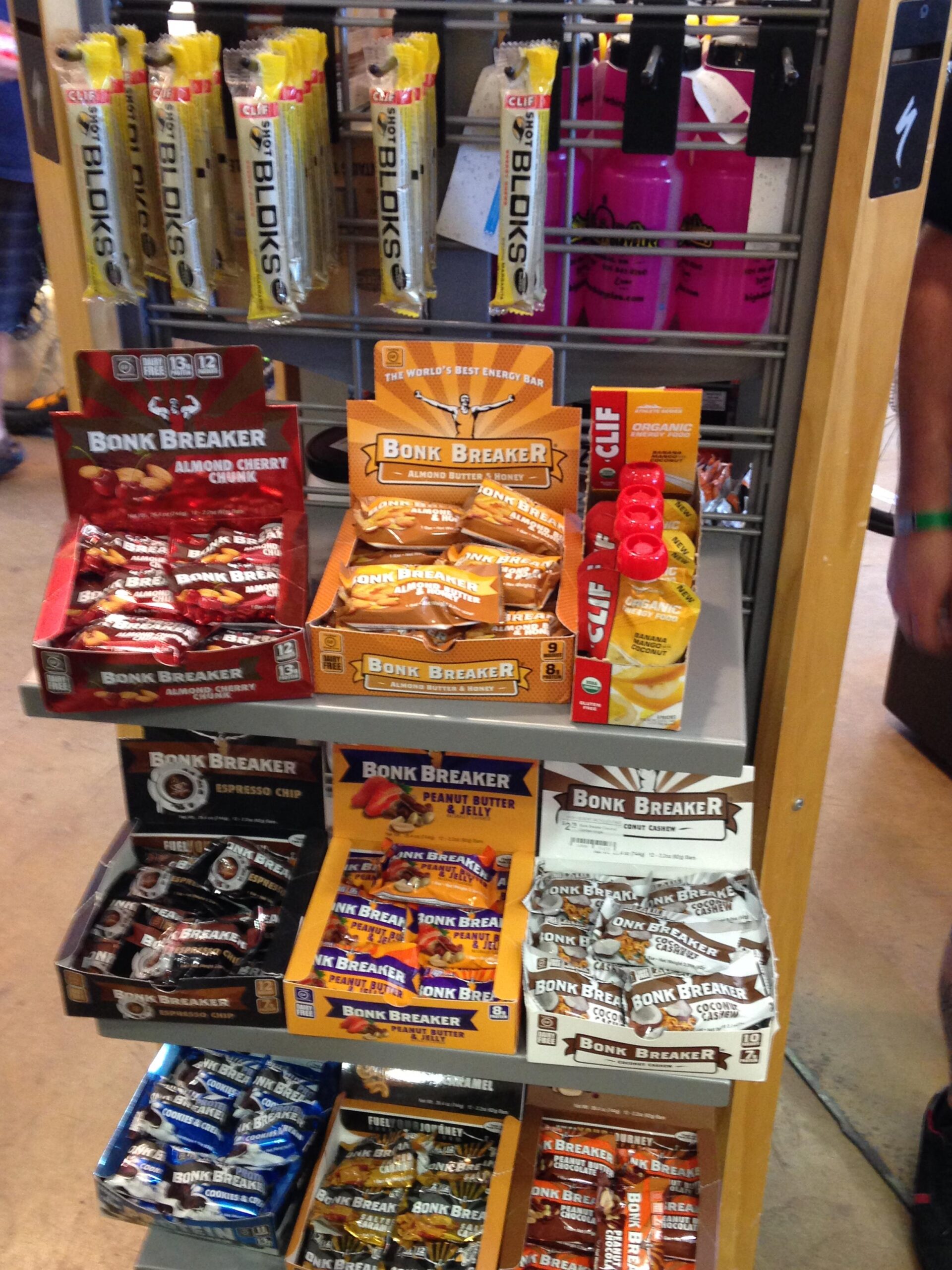 Shelves stocked with a variety of energy snacks, including different flavors of Bonk Breaker bars and Clif Shot Bloks. The display features colorful packaging with flavors such as Almond Cherry Chunk, Peanut Butter & Jelly, and Espresso Chip. Additionally, there are bottles of Clif hydration products visible in the background.
