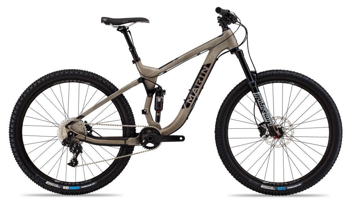 Marin Marin Mount Vision 6: A modern mountain bike with a lightweight brown frame, featuring wide tires and a dual suspension system. The bike is equipped with a black fork and drivetrain components, showcasing advanced gearing and braking systems, making it suitable for off-road riding.