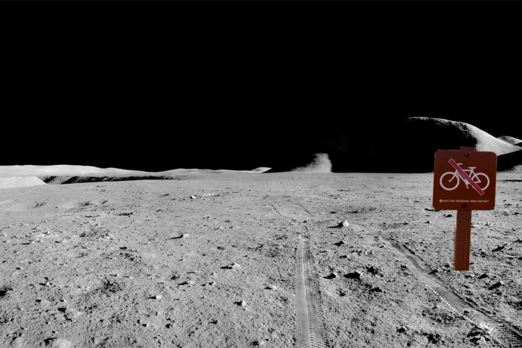 A barren lunar landscape featuring a prominent "No Riding" sign with a bicycle icon and a red slash through it, set against a dark, starry background. Tire tracks are visible in the foreground, indicating previous activity on the surface.