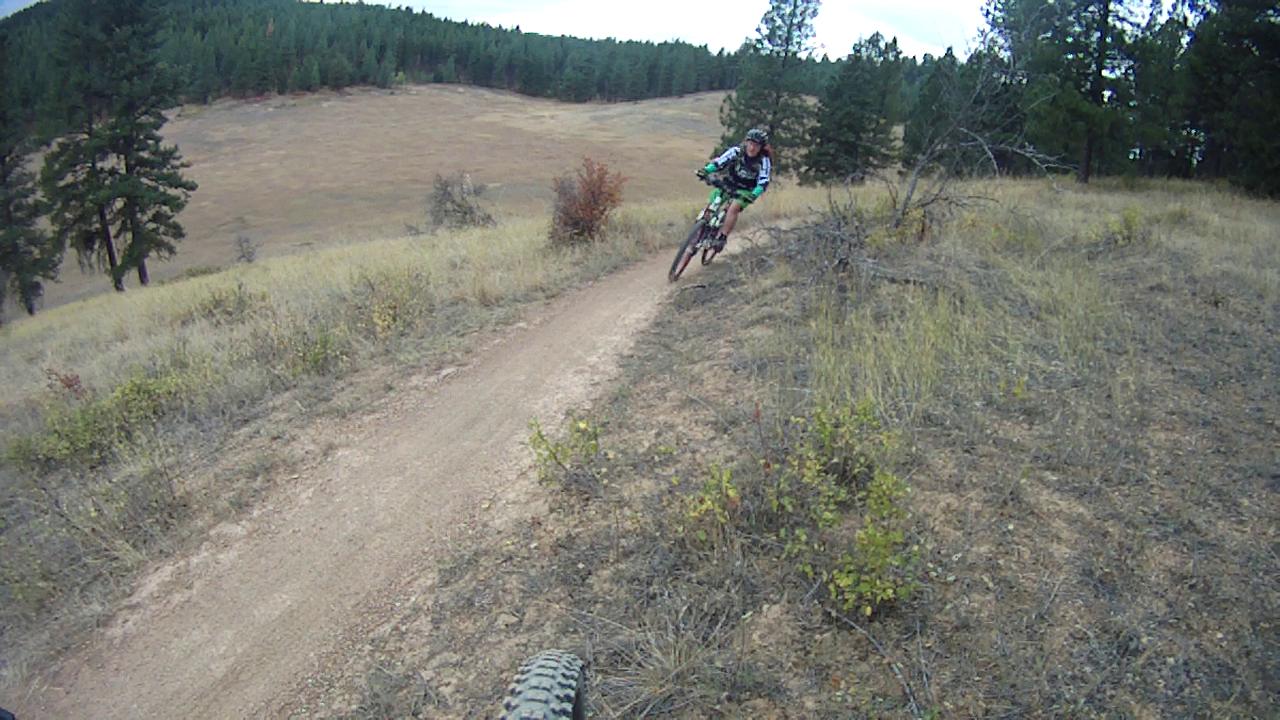 A mountain biker navigating a dirt trail on a hillside, surrounded by trees and open fields, with a focus on the bike and rider in motion. Rattlesnake mountain bike trail.