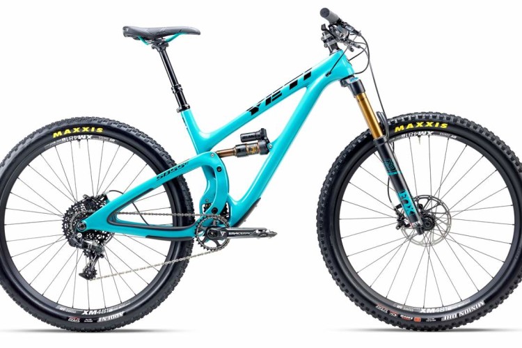 A bright turquoise mountain bike with a modern design, featuring a lightweight frame, front suspension fork, and rugged tires. The bike is positioned at a slight angle, showcasing its drivetrain and quality components, including Maxxis tires. It is displayed against a white background, highlighting its sleek appearance and advanced engineering.