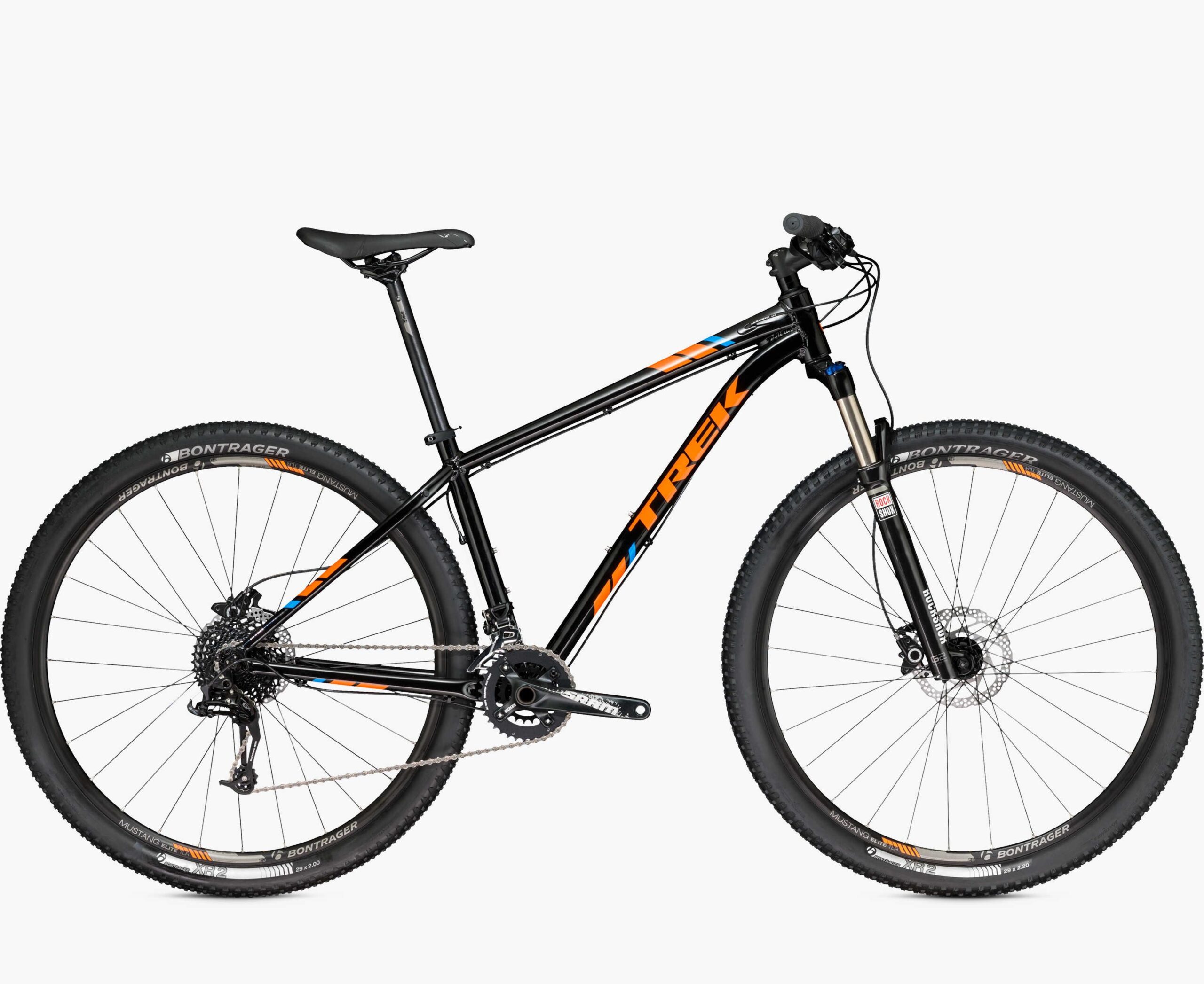 Trek X-Caliber 8: Alt text: A black mountain bike with orange and blue accents, featuring wide tires, a slim seat, and a sturdy frame. The bike is positioned at an angle, showcasing its front suspension and gear system.