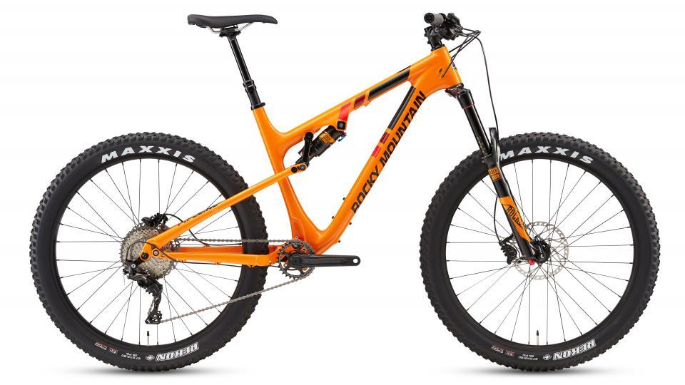 Rocky Mountain Pipeline: Mountain bike with an orange and black frame, featuring Maxxis tires and a suspension system, displayed from the side on a plain background.
