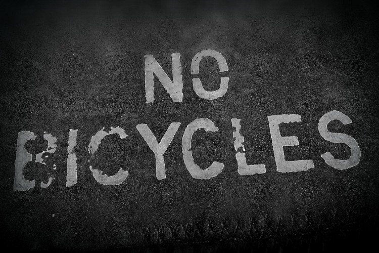 Black and white image of the ground with faded white paint that reads "NO BICYCLES." The background appears textured, contributing to a worn and aged look.