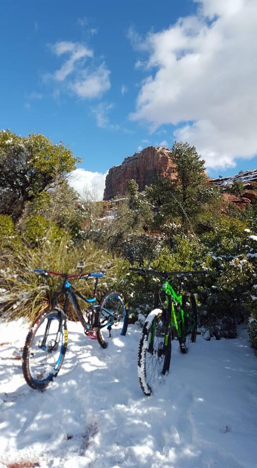 Santa Cruz Bronson: Two mountain bikes are parked in a snowy landscape, surrounded by sparse vegetation and rocky formations under a bright blue sky with scattered clouds.