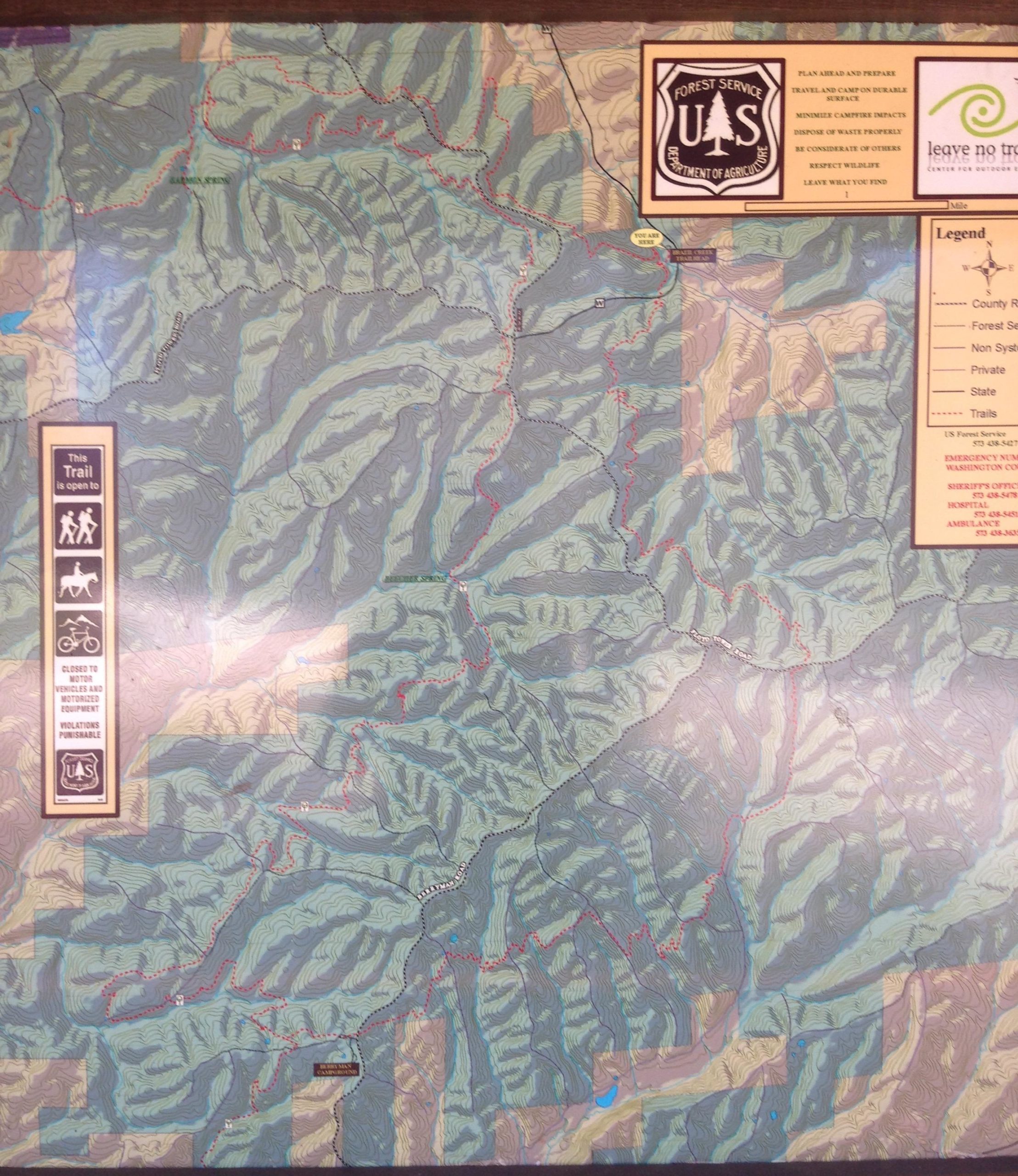 A detailed map displaying various hiking and biking trails in a forested area, featuring topographic lines and shaded relief to indicate elevation changes. The map includes symbols for trail access and usage, along with a legend outlining different land types and restrictions. Notable markings indicate distances and specific routes, along with official seals from the U.S. Forest Service. Berryman mountain bike trail.