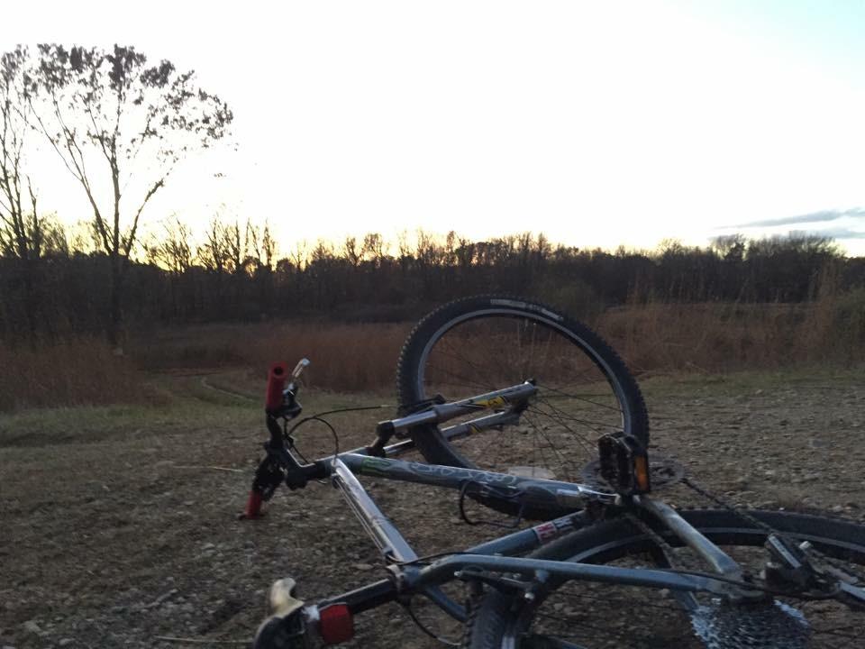 Gary Fisher Tassajara: A mountain bike lying on its side with the foreground showing its wheels and frame. The background features a barren landscape with trees silhouetted against a softly lit sky during sunset.