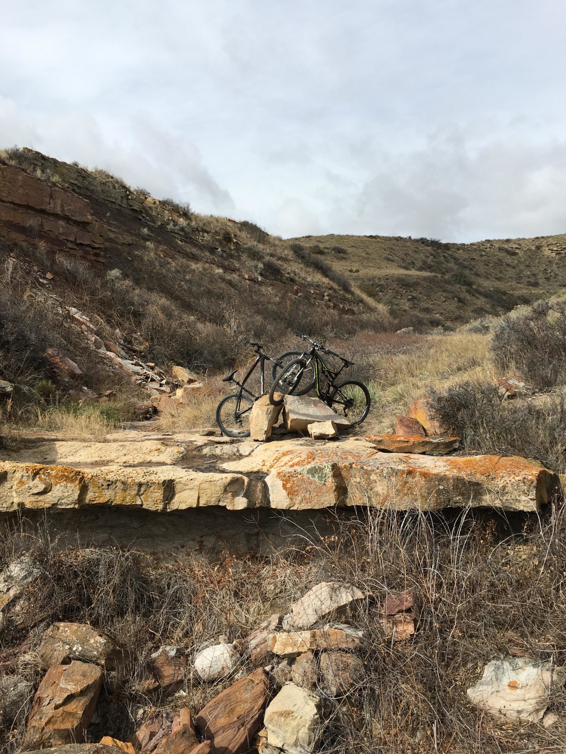 A mountain bike resting on a large rock outcrop in a dry, grassy landscape with rolling hills and cloudy skies in the background. North Shore mountain bike trail.