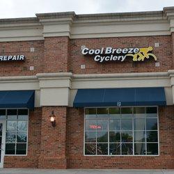 Exterior view of the Cool Breeze Cyclery store, featuring a brick facade, large windows, and blue awnings. The signage prominently displays the store name, with “Cool Breeze Cyclery” in bold lettering, alongside a bicycle icon. Nearby, there is a sign indicating bicycle repair services.
