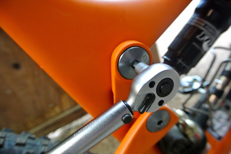 Close-up image of a silver ratchet wrench attached to an orange bicycle frame, showcasing the tool against the smooth finish of the frame and surrounding bicycle components.