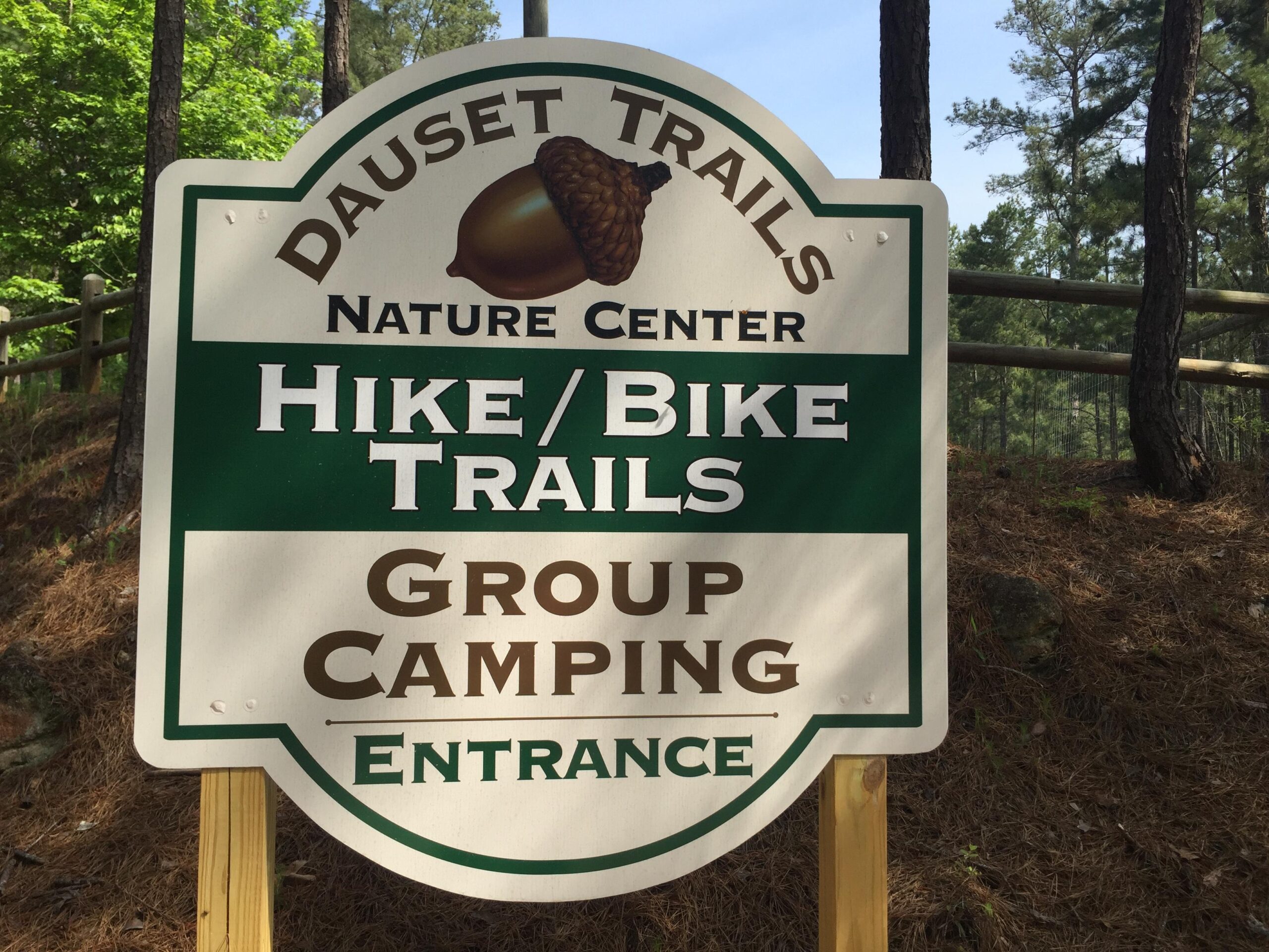 Sign for Dauset Trails Nature Center indicating the entrance for Hike/Bike Trails and Group Camping. The sign features an acorn graphic and is surrounded by trees. Dauset Trails Nature Center mountain bike trail.