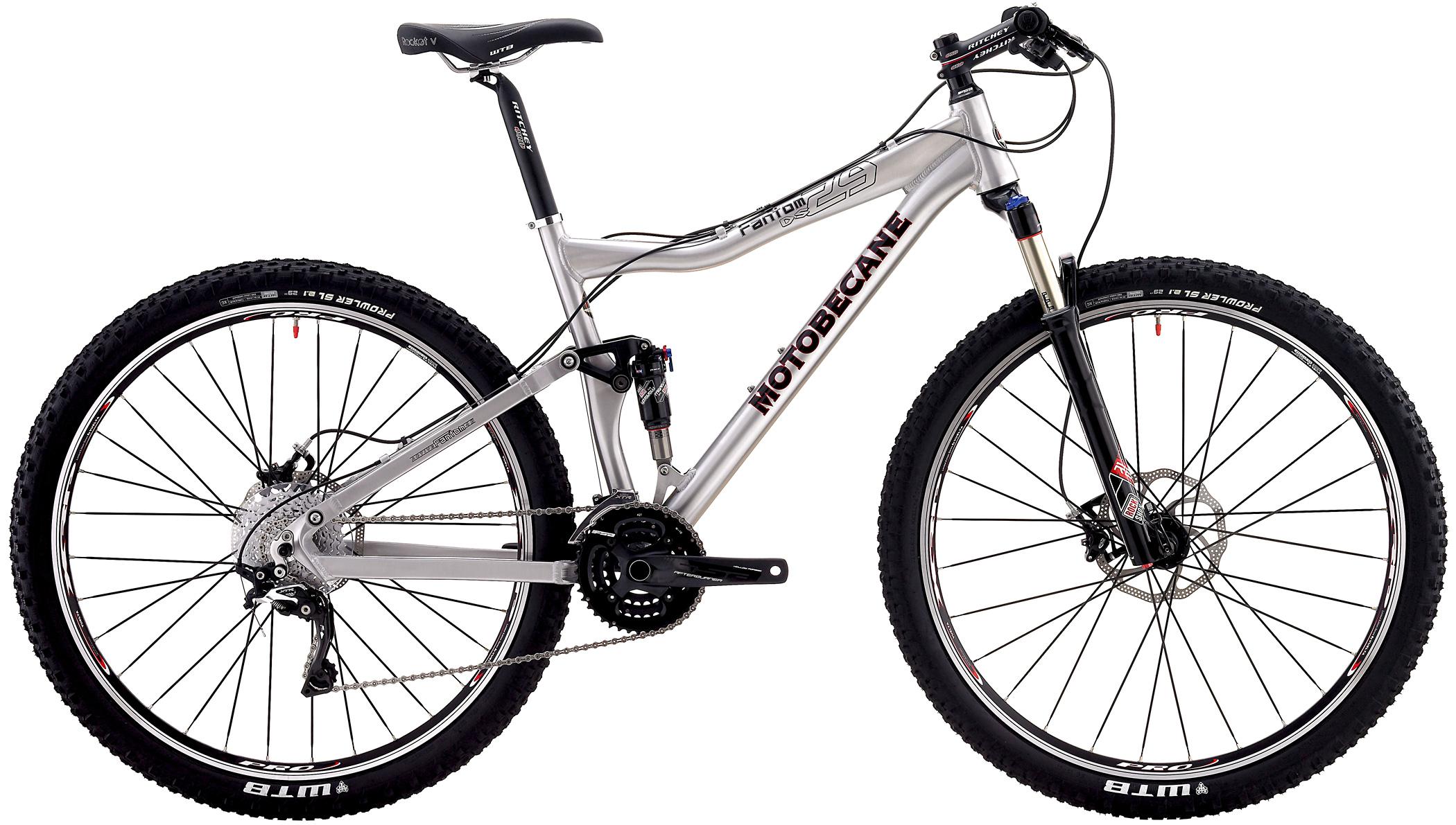 Motobecane Fantom 29 FS: A silver Motobecane mountain bike featuring a dual suspension system, wide tires with aggressive tread for off-road traction, and a variety of gears for varied terrain. The bike has a sleek design, including a black saddle and handlebars, and is positioned against a plain white background.