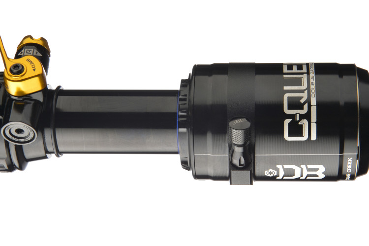 A black and gold mountain bike shock absorber, showcasing a sleek design. The shock features adjustable settings, including a yellow lever and various knobs for tuning. It is labeled with the brand name "C-QUE" and model "D3" for precise identification.