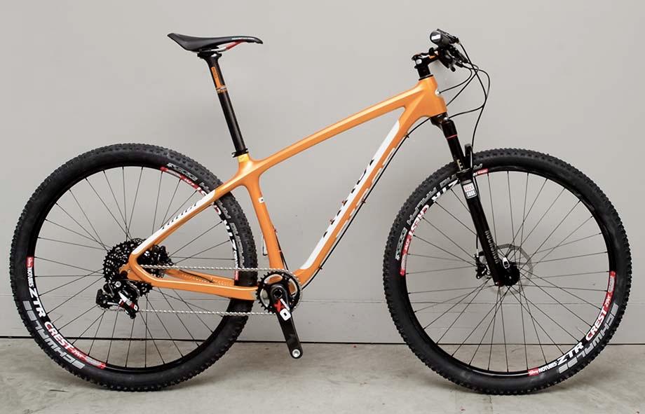 Niner Air 9 Carbon: Alt text: A sleek orange mountain bike with black components, featuring wide tires suitable for off-road terrain, standing against a neutral background.