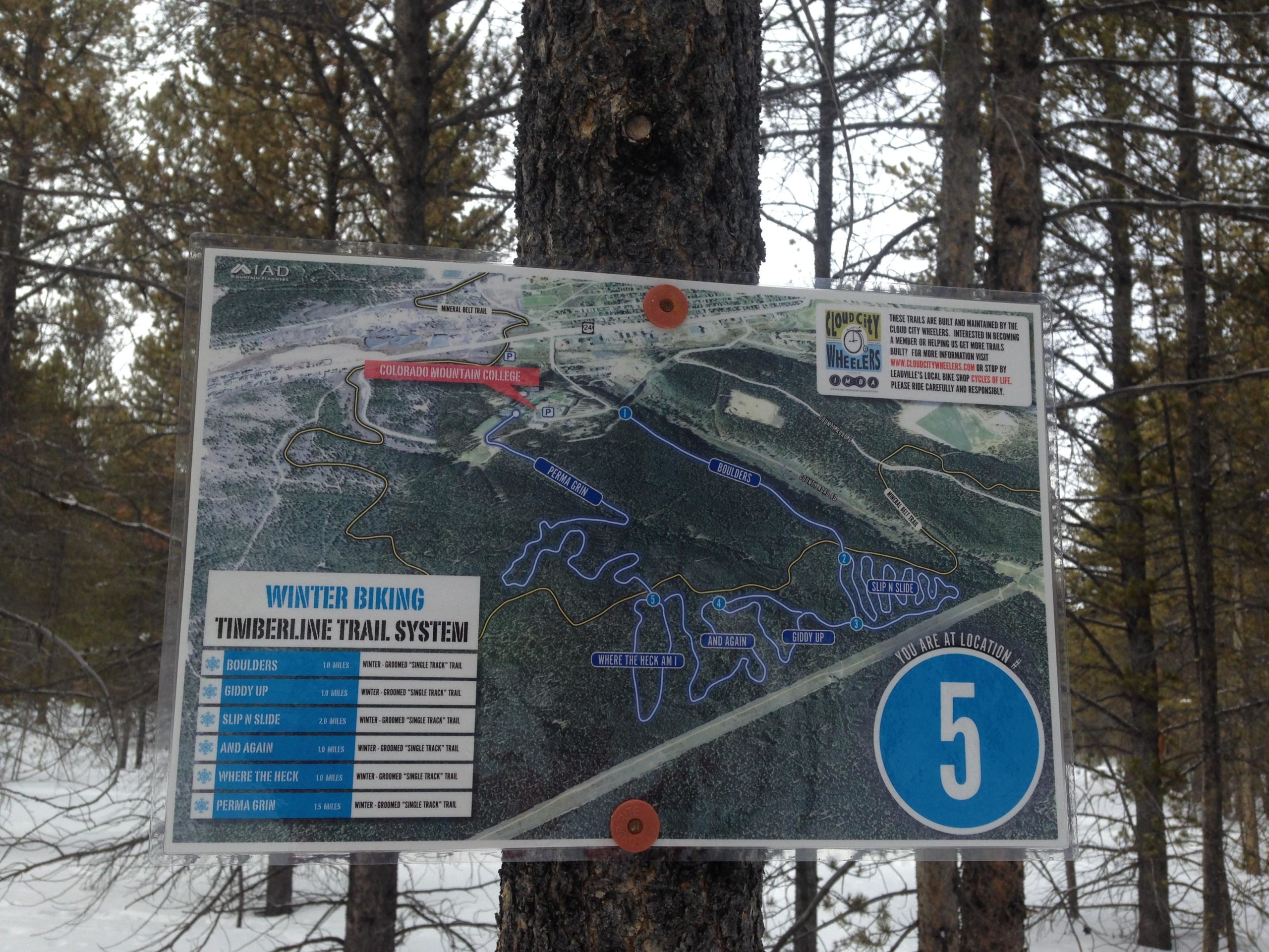 Map of the Timberline Trail System for winter biking, featuring trail names and distances, and indicating the current location as number 5. The map includes winter biking trail designations such as "Boulders," "Giddy Up," and "Slip n Slide," and is situated on a tree in a snowy forested area. Colorado Mountain College Trails mountain bike trail.