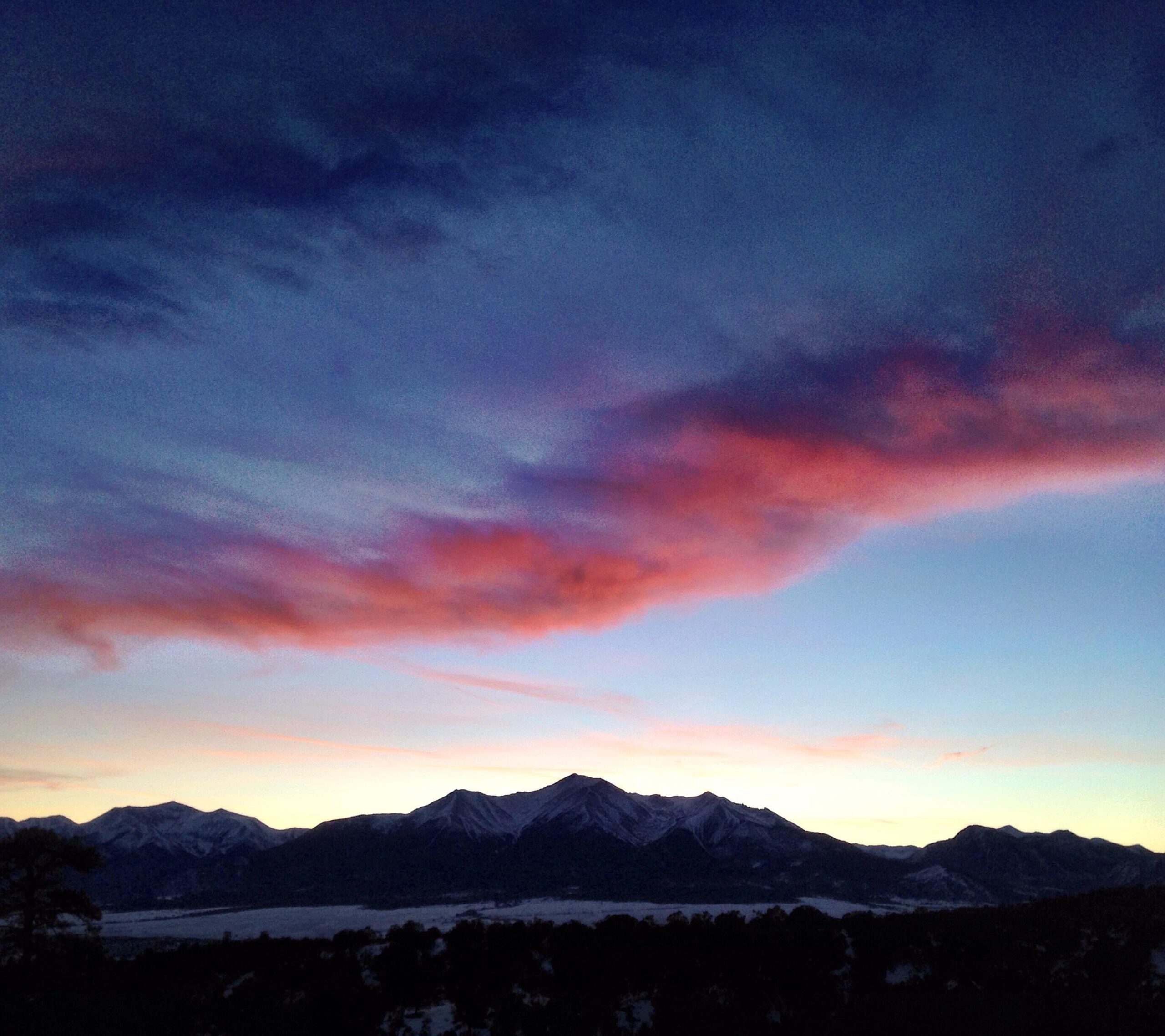 A serene landscape featuring mountains silhouetted against a twilight sky, with vibrant pink and purple clouds contrasting against a deep blue background. The scene captures the tranquil beauty of nature at dusk. Midland Hills Trails mountain bike trail.
