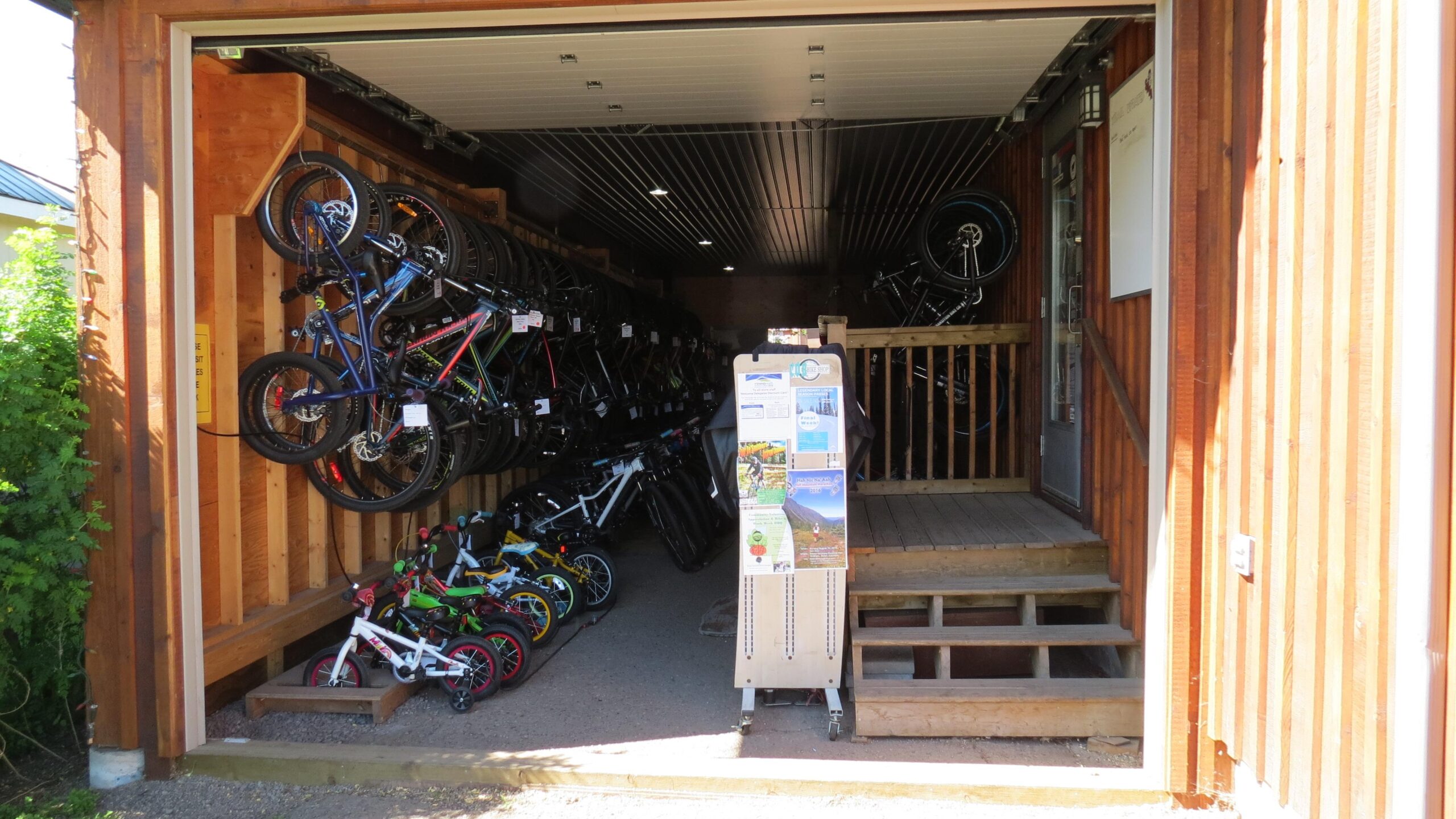 Alt tag: A bike rental shop entrance featuring an assortment of bicycles displayed on racks inside, with colorful children's bikes visible in the foreground and informational brochures on a stand near the entrance.