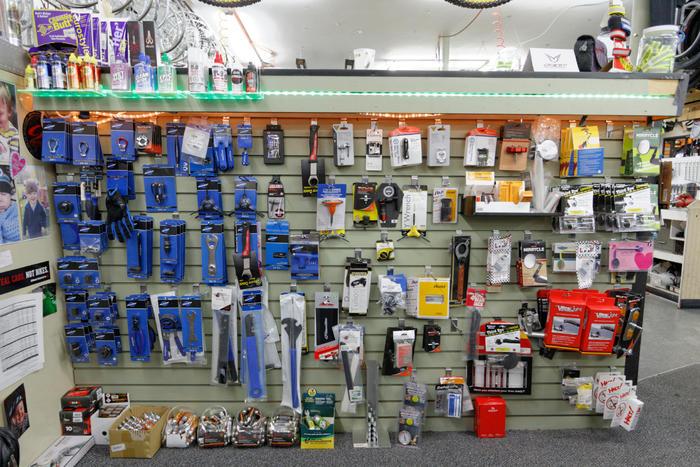 A display wall showcasing a variety of tools and accessories organized by category, featuring products in blue packaging, safety gloves, measuring devices, and battery packs, set against a green slatwall background.