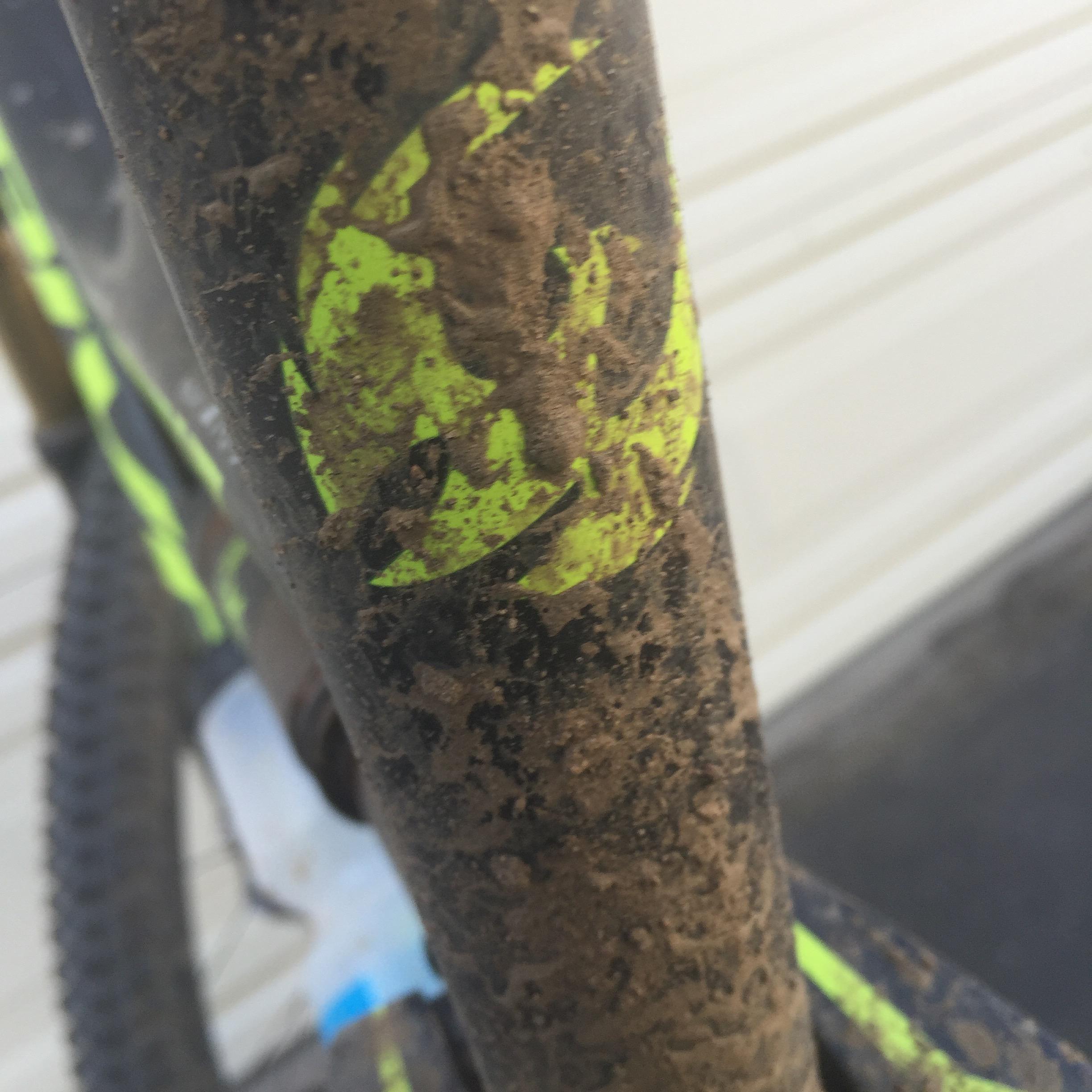 Pivot Mach 429SL Carbon: Close-up of a muddy bicycle frame featuring a bright yellow logo, highlighting dirt and grime accumulated after use.