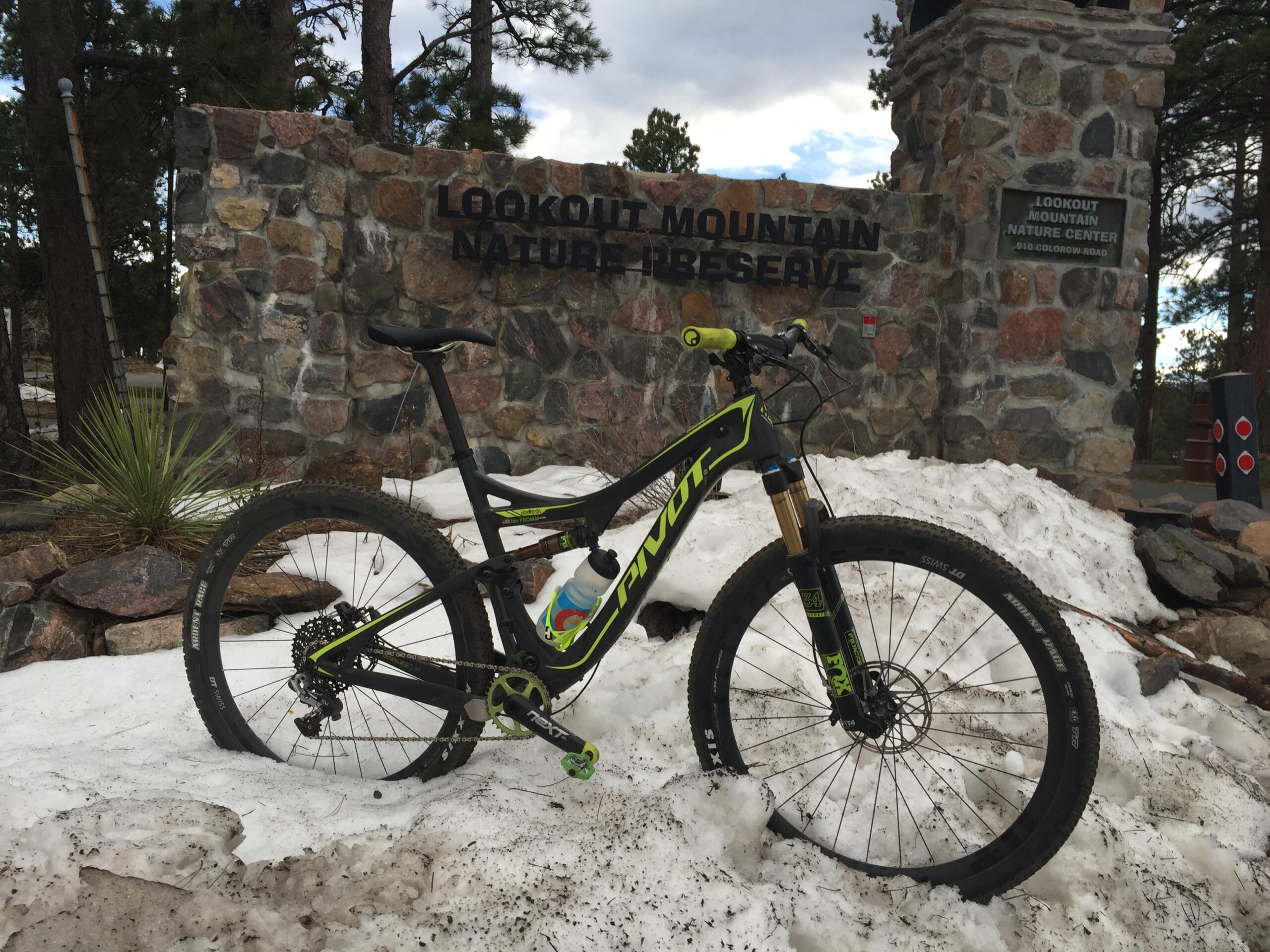 Pivot Mach 429SL Carbon: A mountain bike leaning against a stone sign for Lookout Mountain Nature Preserve, with patches of snow on the ground and pine trees in the background.