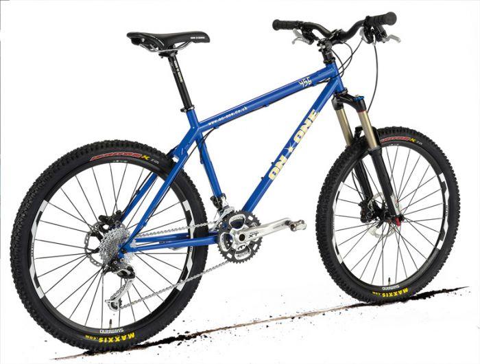 On-One 456: A blue mountain bike with large knobby tires, a lightweight aluminum frame, and front suspension forks, positioned on a white background. The bike features multiple gears, a sleek design, and is equipped for off-road cycling.